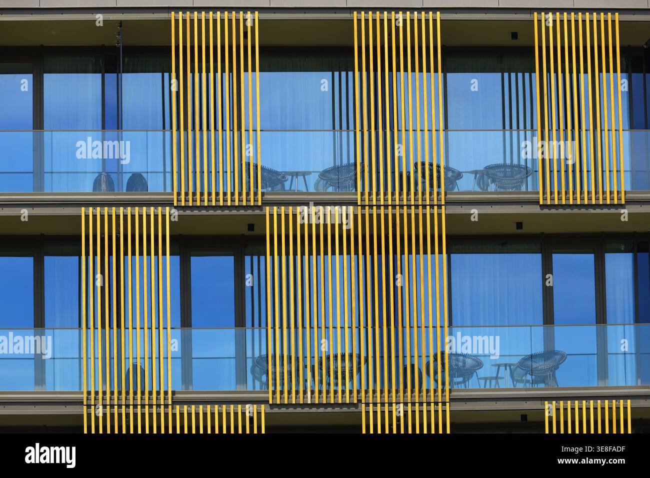 Modernes Apartmentgebäude mit sich wiederholenden Balkonen mit Glasgeländern und vertikalen architektonischen Elementen, die eine auffällige geometrische Fassade mit hohem Glanz schaffen Stockfoto