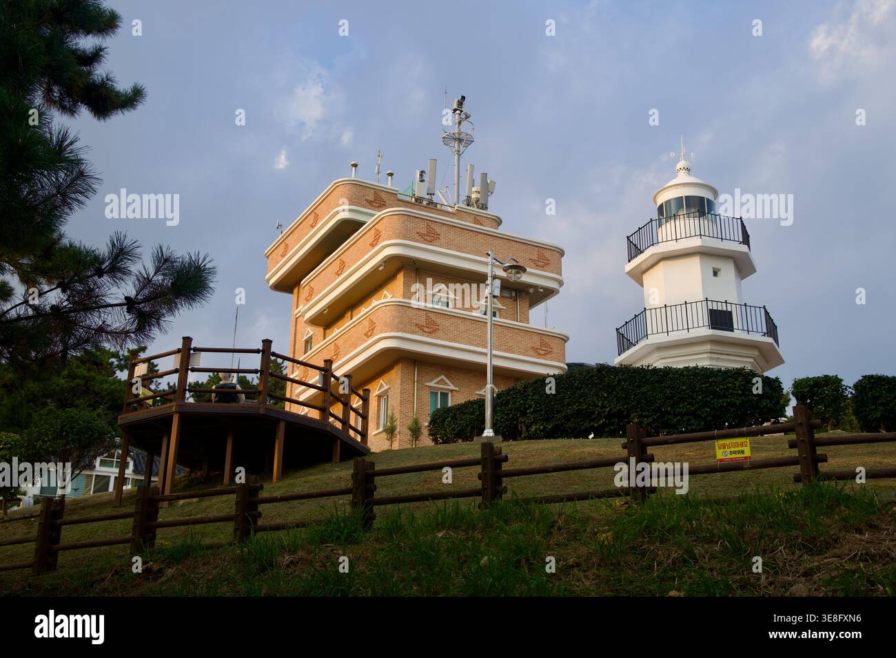 Das Ulgi Lighthouse befindet sich neben dem Backsteingebäude im Daewangam Park mit einer Holzterrasse und einem umzäunten Rasen am Hügel darunter. Stockfoto