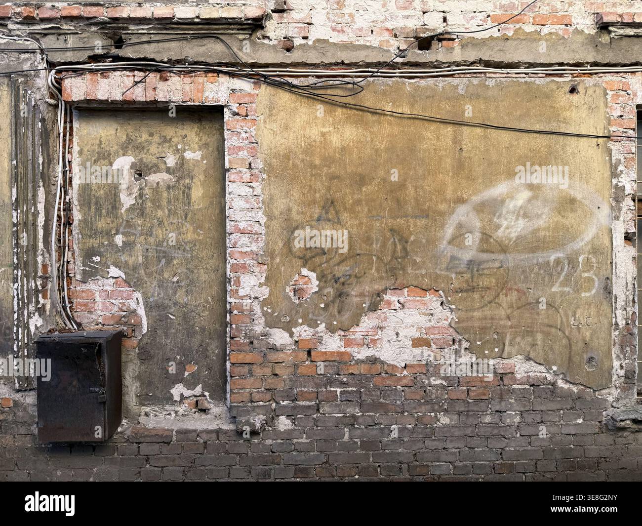 Alte zerstörte Mauer eines verlassenen Ziegelgebäudes mit Metallkästen und Kabeln Stockfoto