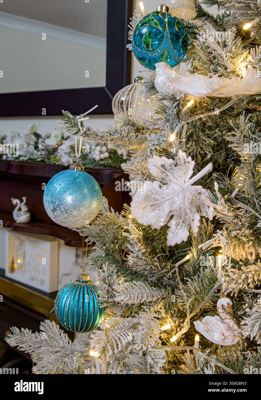 Nahaufnahme von blauen und weißen Weihnachtskugeln und Dekorationen auf mattierten Ästen mit warmen Feenlichtern und festlichem Innenraum Stockfoto