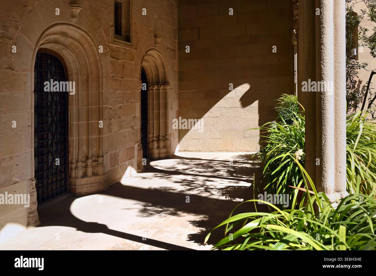 Sonnendurchfluteter Kreuzgang mit Steinbögen, tiefen Schatten und üppigen Innenhofpflanzen, im Kloster Montserrat, Katalonien, Spanien Stockfoto