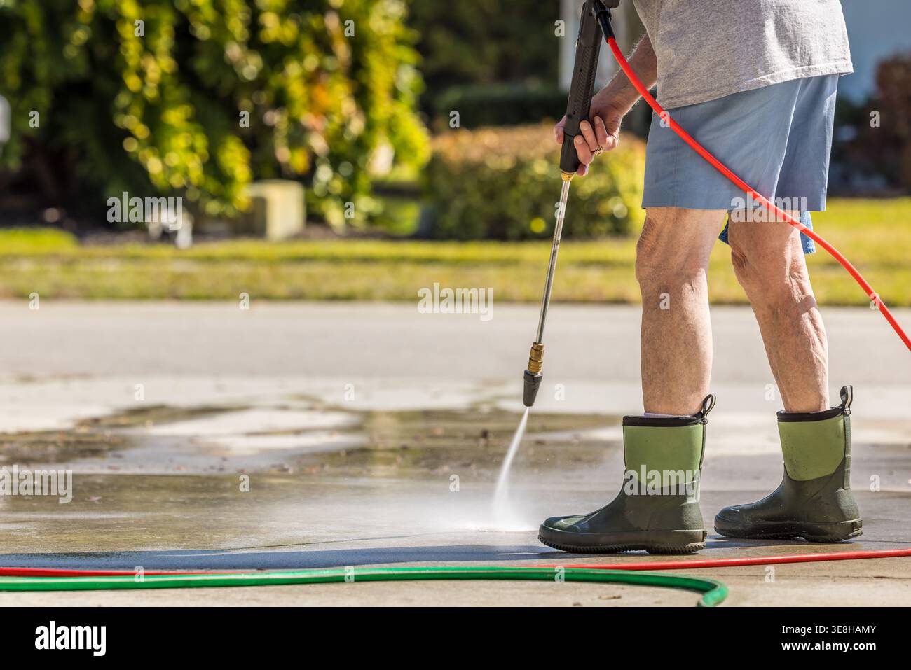 Mann mit Hochdruckreiniger, um Wohnbeton-Bürgersteig zu waschen. Stockfoto