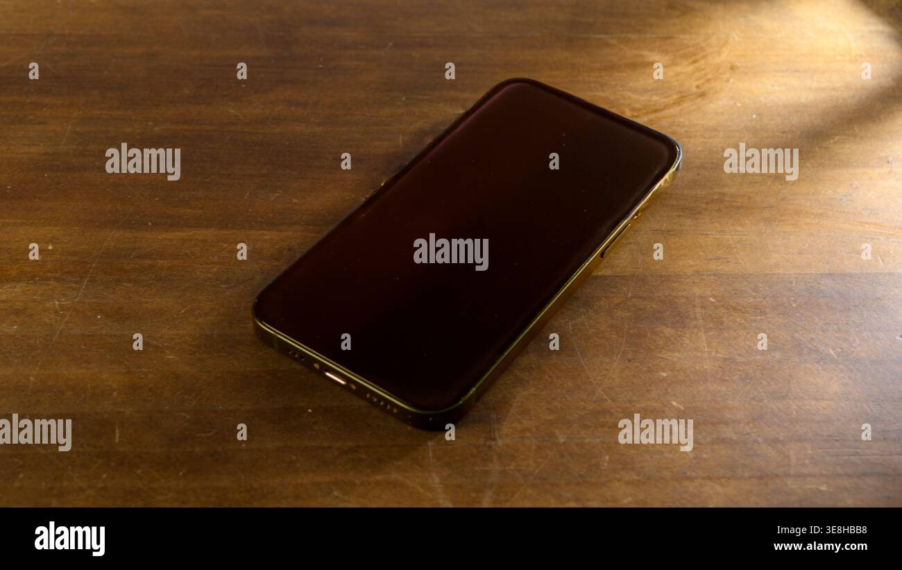 Smartphone auf Holzschreibtisch mit warmem Licht, minimaler Einrichtung für mobile Produktivität und digitalen Lifestyle Stockfoto