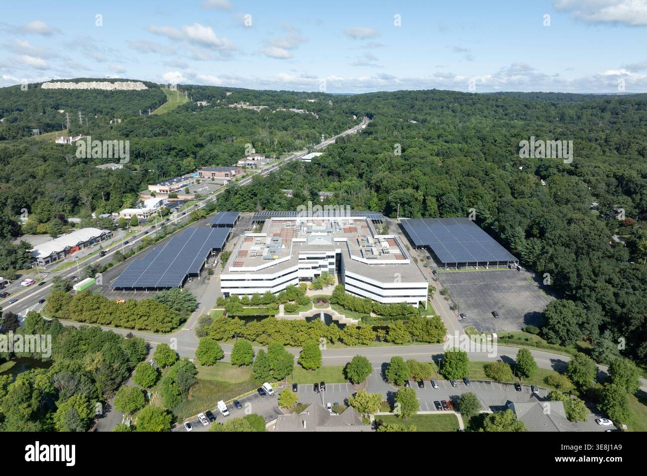 Blick aus der Vogelperspektive auf einen solargetäfelten Büropark, umgeben von bewaldeten Hügeln in Morris Plains, New Jersey. Stockfoto