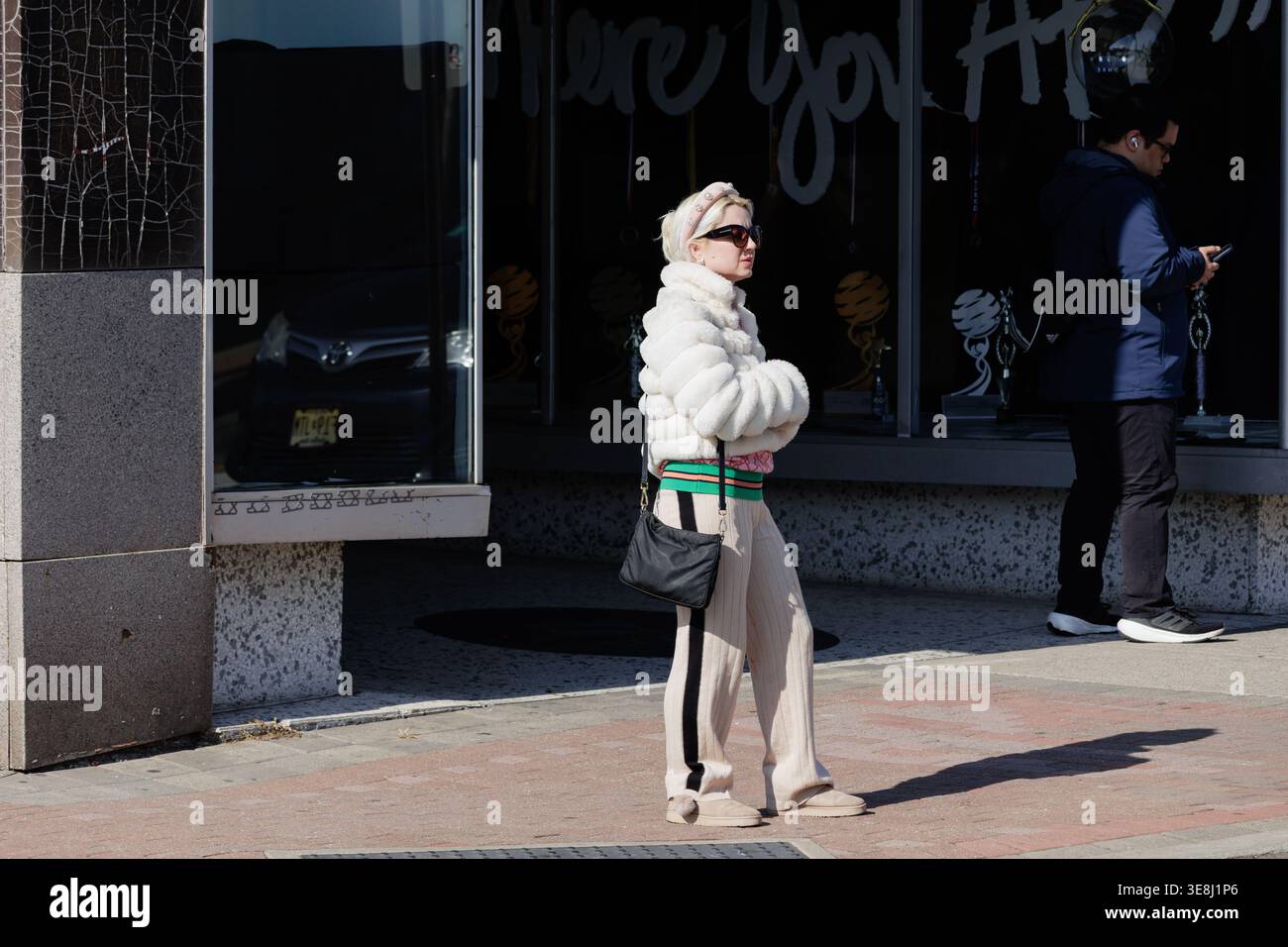 Eine stilvoll gekleidete Frau in einer weißen Kunstpelzjacke und einer Hose mit weitem Bein steht auf einem Bürgersteig in Bergenfield, New Jersey. Stockfoto