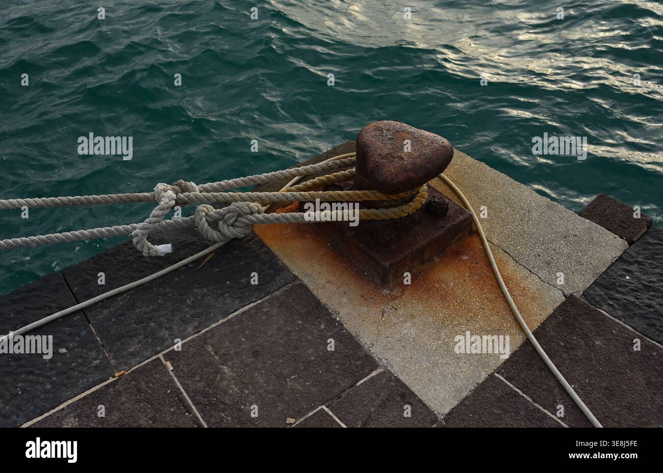 Rostiger Schiffspoller mit Seil am Pier am Ufer in Ortigia, Sizilien Stockfoto