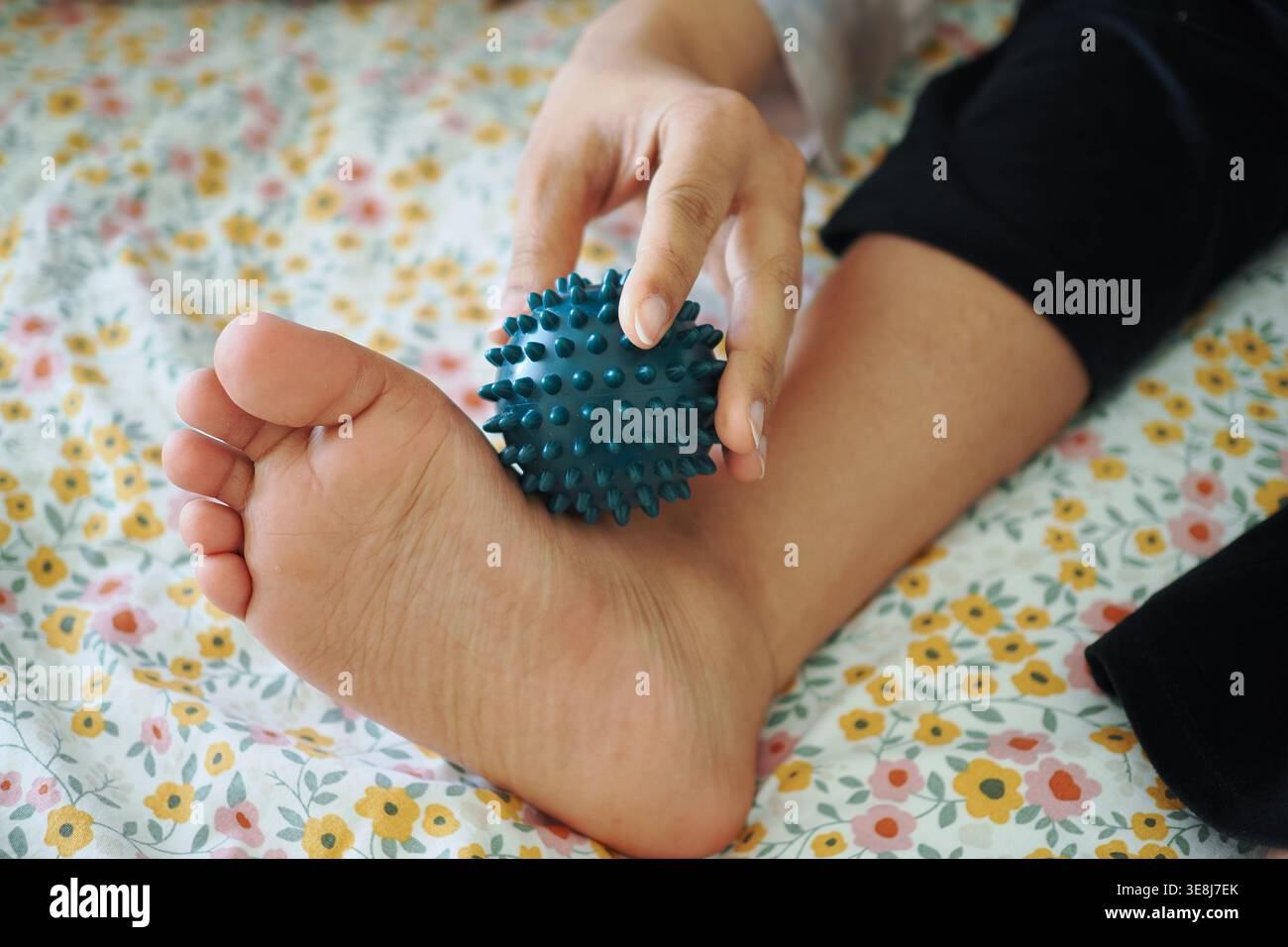 Fußmassage an einem Kinderfuß mit einem stacheligen Ball auf weicher Oberfläche Stockfoto