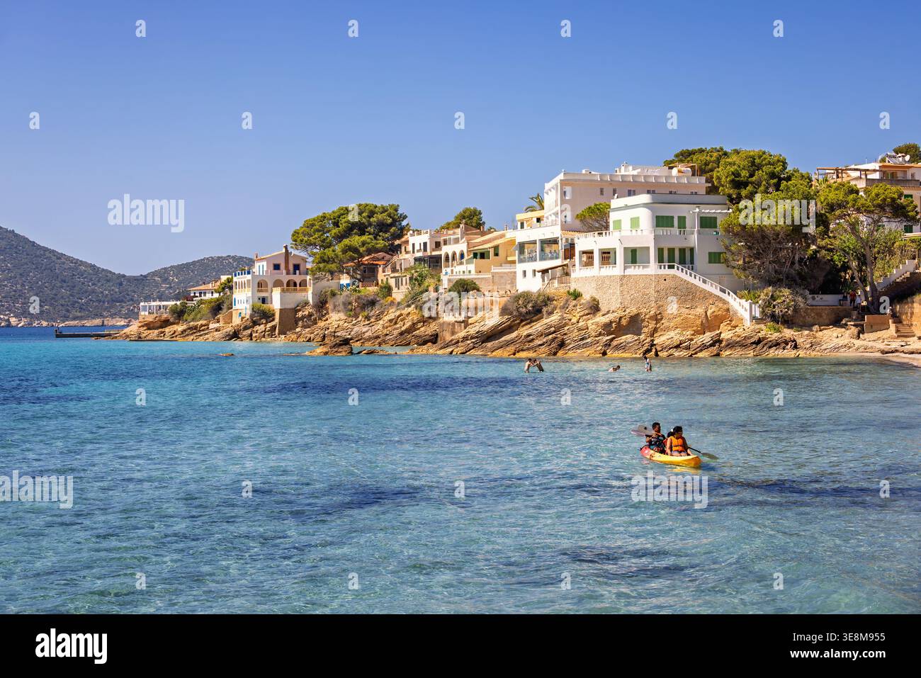 Strandhäuser am felsigen Ufer mit Leuten, die Kajaks paddeln und im Meer schwimmen Stockfoto