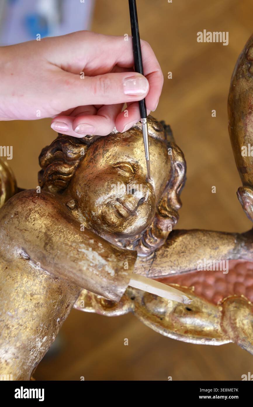 Eine Person arbeitet mit einem kleinen Pinsel, um Blattgold an einer Holzschnitzerei in einem Kunststudio bei Tageslicht zu bearbeiten. Stockfoto