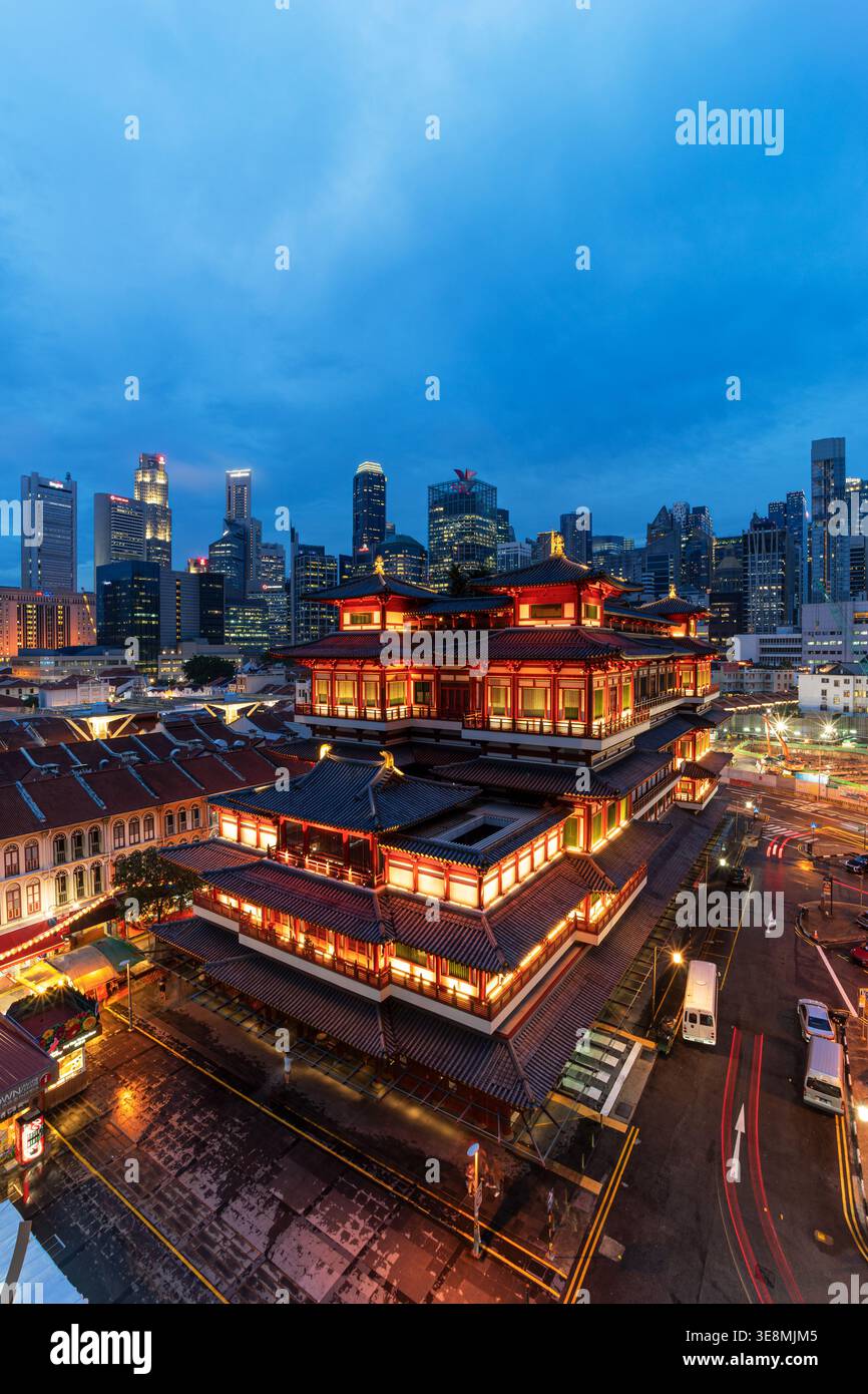 Beleuchteter Buddha Tooth Relic Tempel in Chinatown, Singapur bei Nacht, mit Ampelpfaden und der modernen Skyline der Stadt dahinter. Kategorien Stockfoto