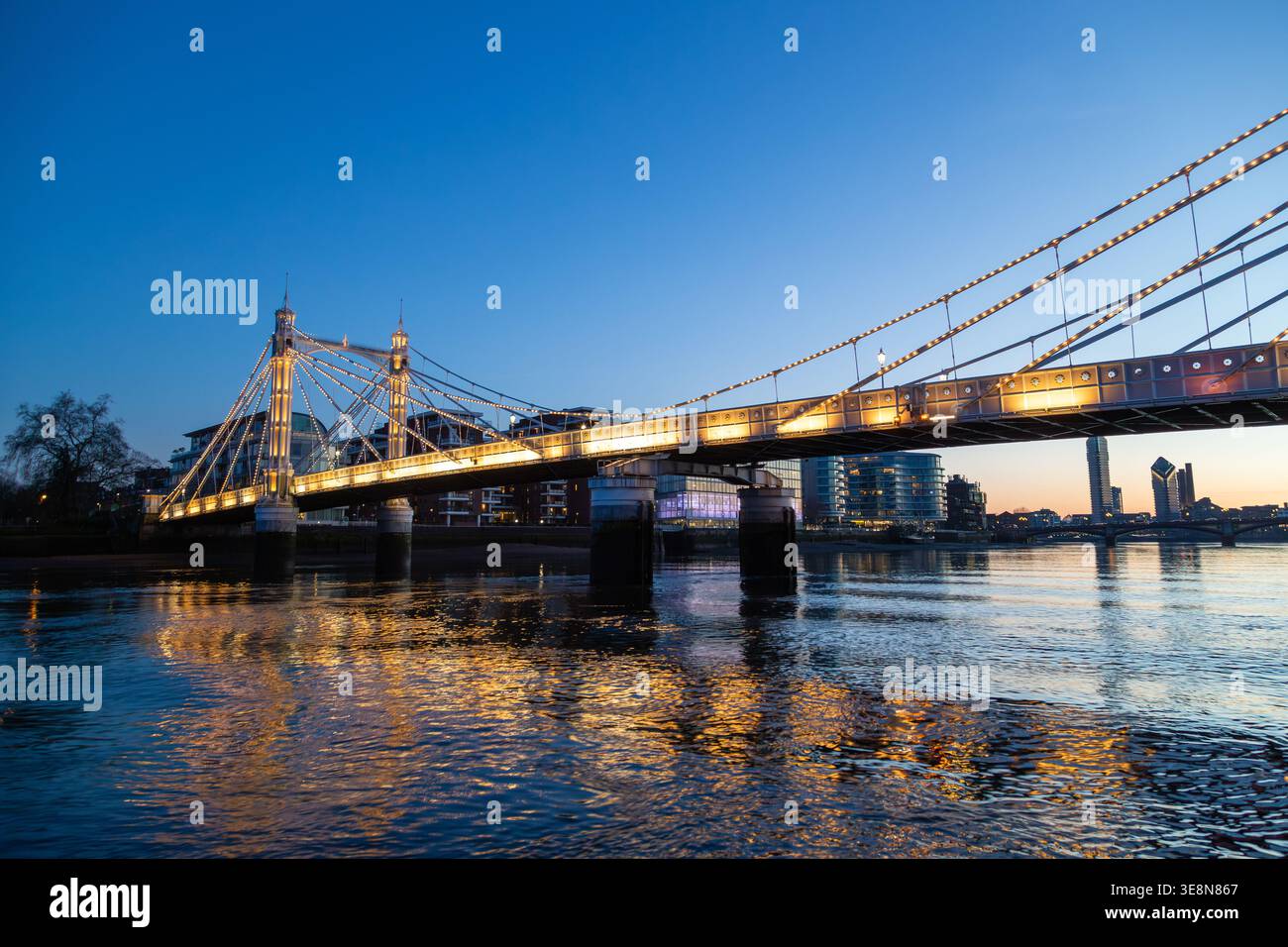 Die Albert Bridge wird nachts beleuchtet, ihre Lichter reflektieren die Themse von einem Uber-Boot auf der Themse. Stockfoto