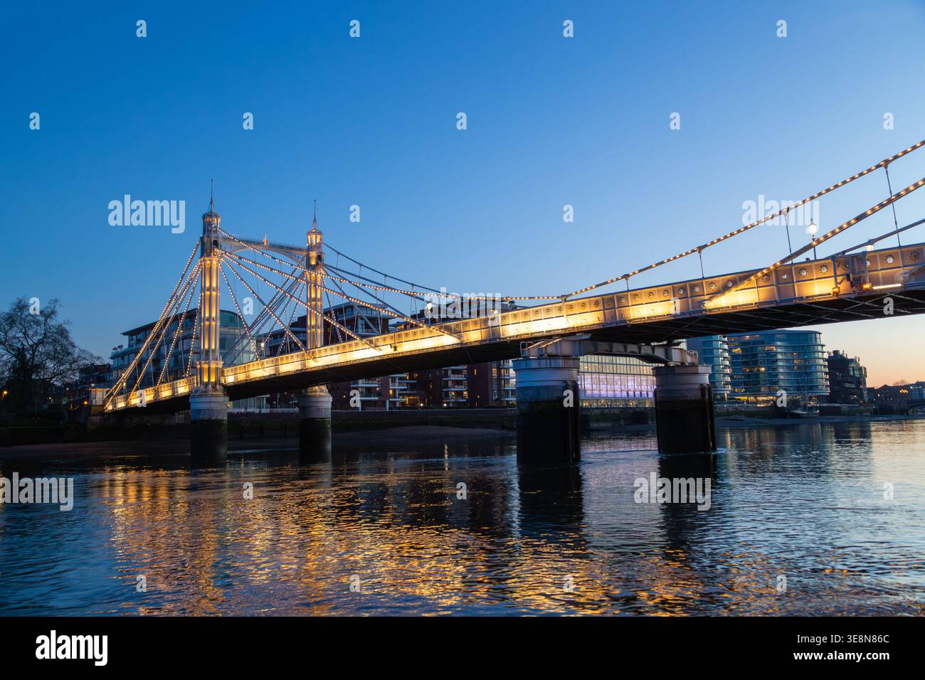 Die Albert Bridge wird nachts beleuchtet, ihre Lichter reflektieren die Themse von einem Uber-Boot auf der Themse. Stockfoto