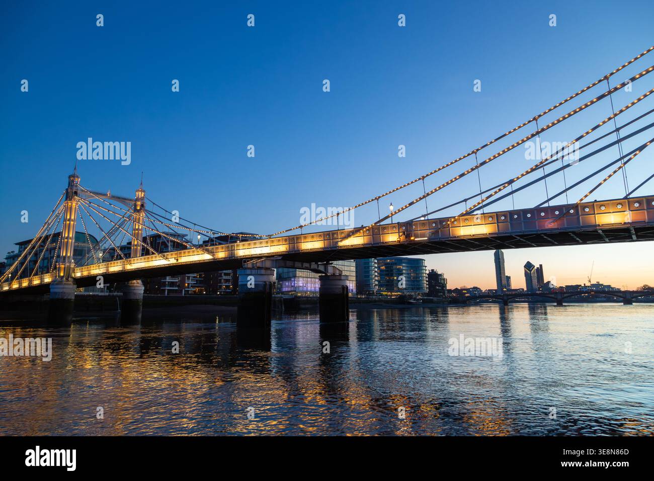 Die Albert Bridge wird nachts beleuchtet, ihre Lichter reflektieren die Themse von einem Uber-Boot auf der Themse. Stockfoto