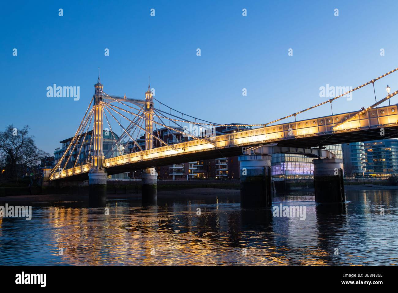 Die Albert Bridge wird nachts beleuchtet, ihre Lichter reflektieren die Themse von einem Uber-Boot auf der Themse. Stockfoto