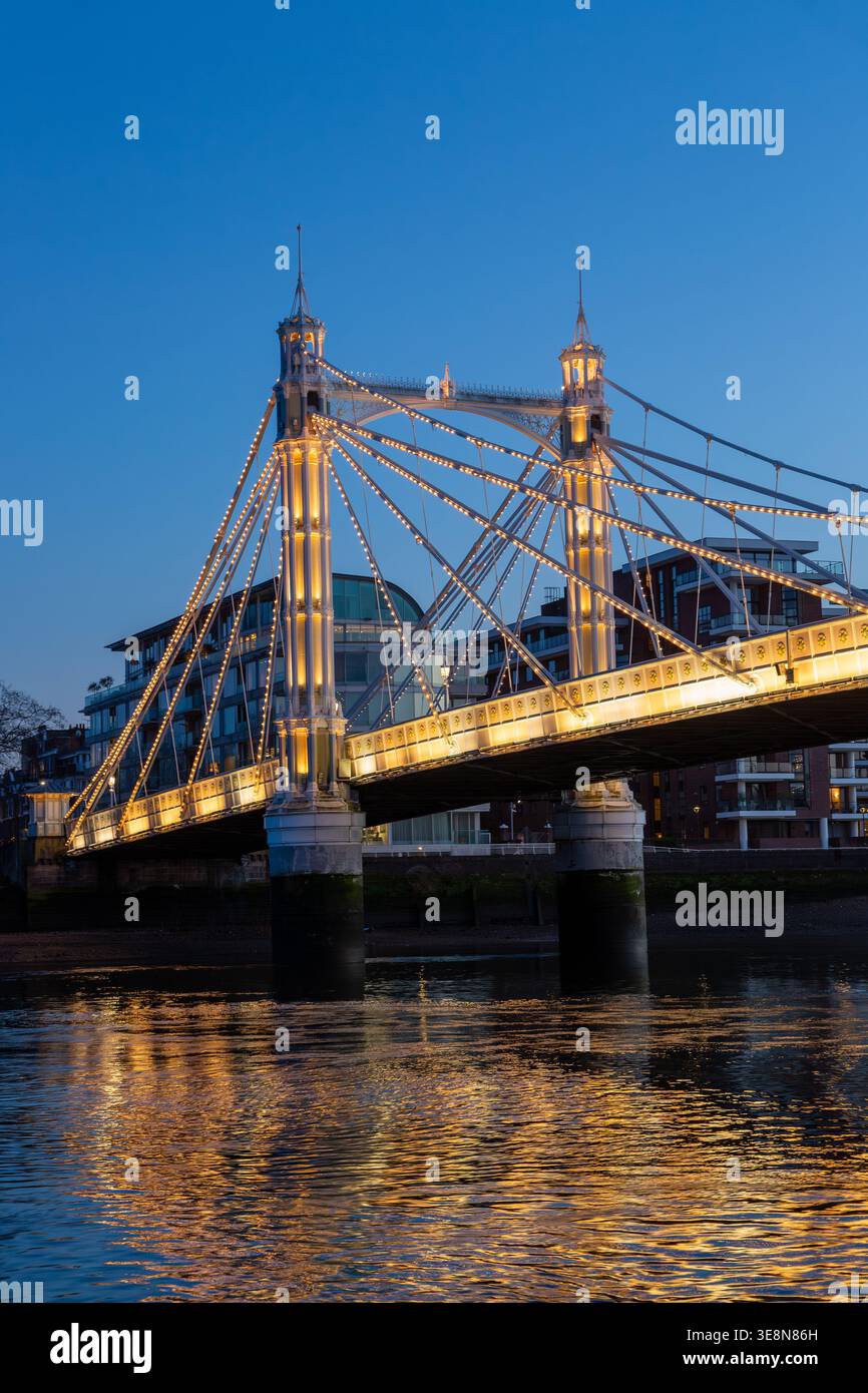 Die Albert Bridge wird nachts beleuchtet, ihre Lichter reflektieren die Themse von einem Uber-Boot auf der Themse. Stockfoto