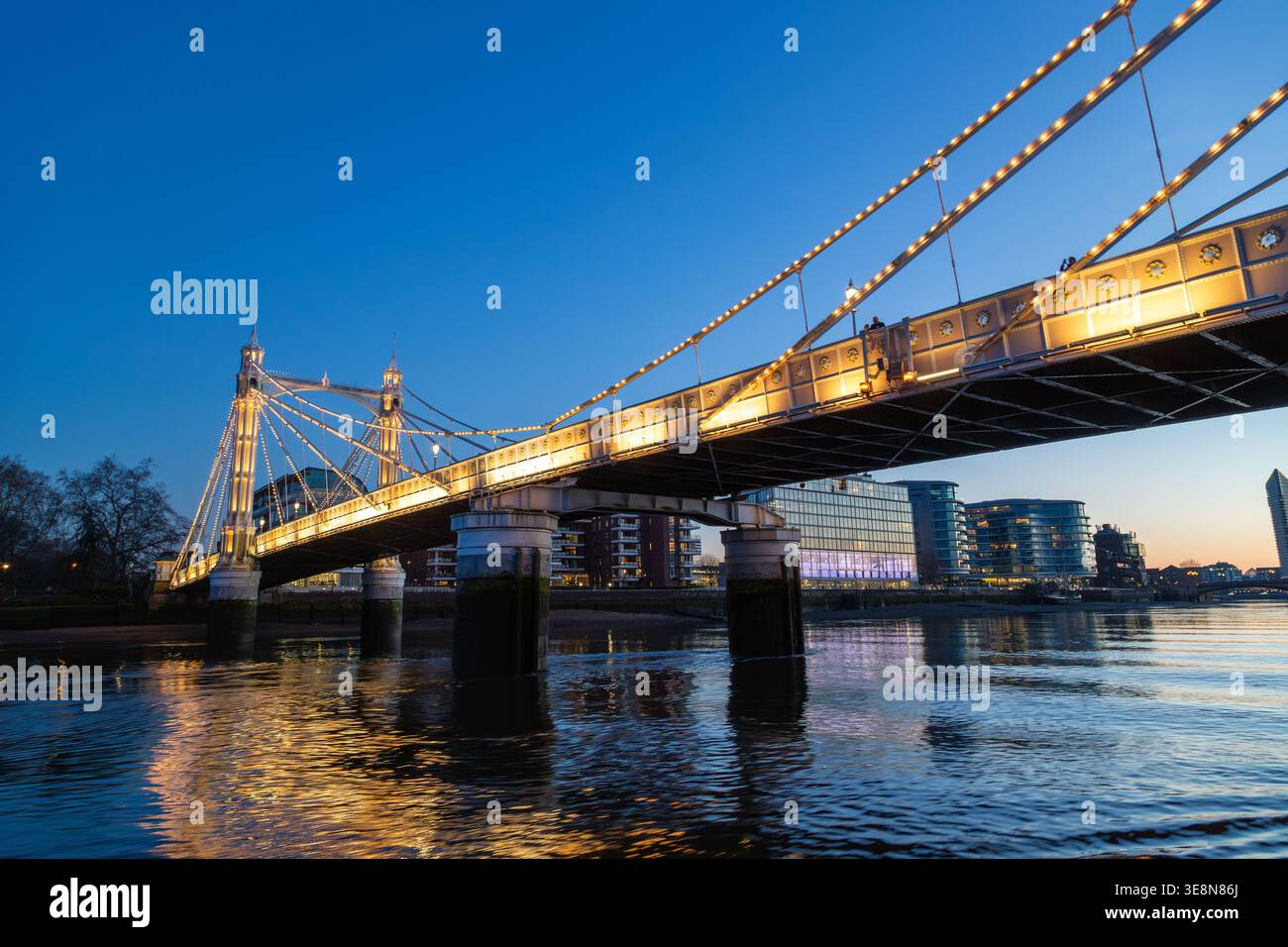 Die Albert Bridge wird nachts beleuchtet, ihre Lichter reflektieren die Themse von einem Uber-Boot auf der Themse. Stockfoto