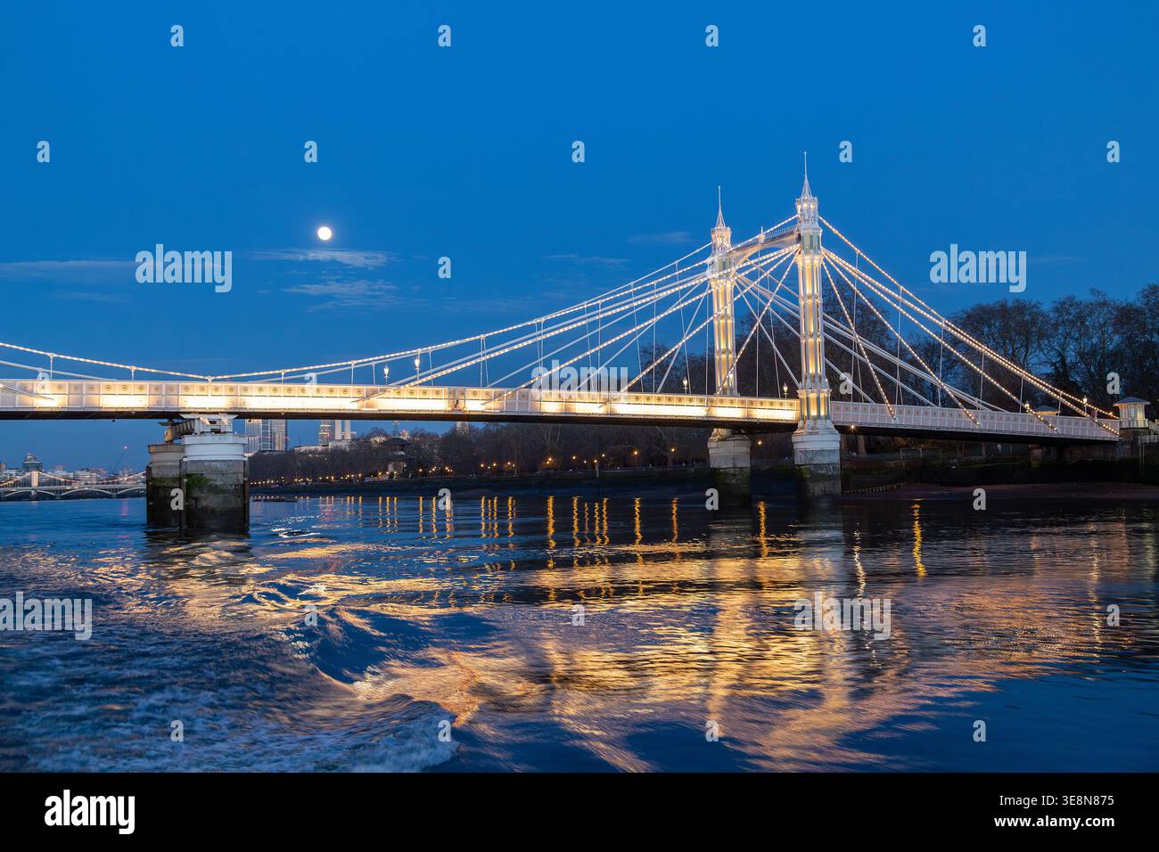 Die Albert Bridge wird nachts beleuchtet, ihre Lichter reflektieren die Themse von einem Uber-Boot auf der Themse. Stockfoto