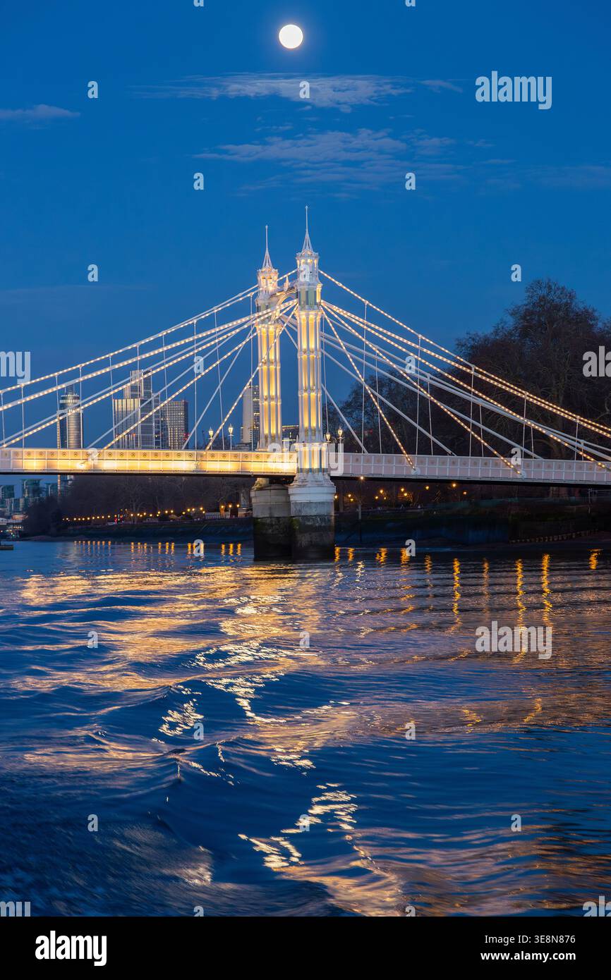 Die Albert Bridge wird nachts beleuchtet, ihre Lichter reflektieren die Themse von einem Uber-Boot auf der Themse. Stockfoto