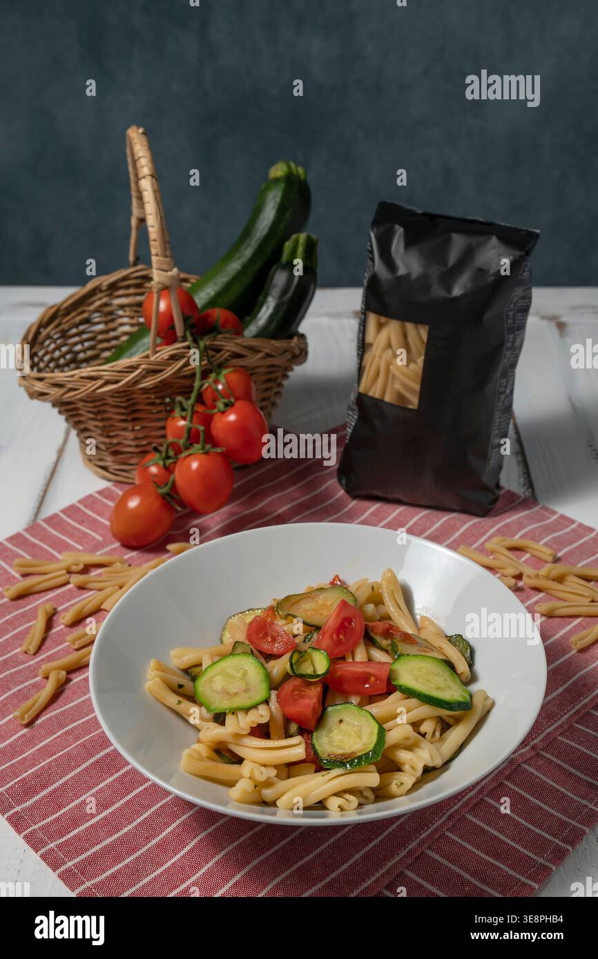Ein Teller mit Pasta, Caserecce mit Tomaten und Zucchini, dazu ein halbes Kilo-Paket und die Zutaten, die in der Nähe verwendet werden Stockfoto