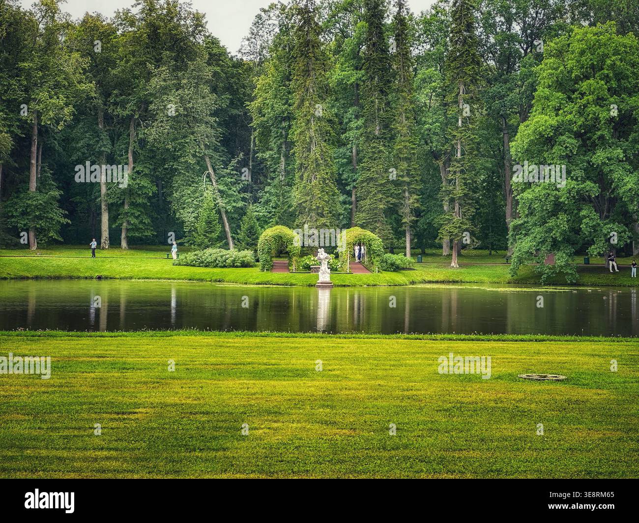 Malerischer Teich mit Reflexionen und Ziergarten im Peterhof Park, Sankt Petersburg. Grüne Landschaft mit Bäumen, Skulpturen und friedlicher Atmosphäre - Smartphone-aufgenommenes Stockfoto