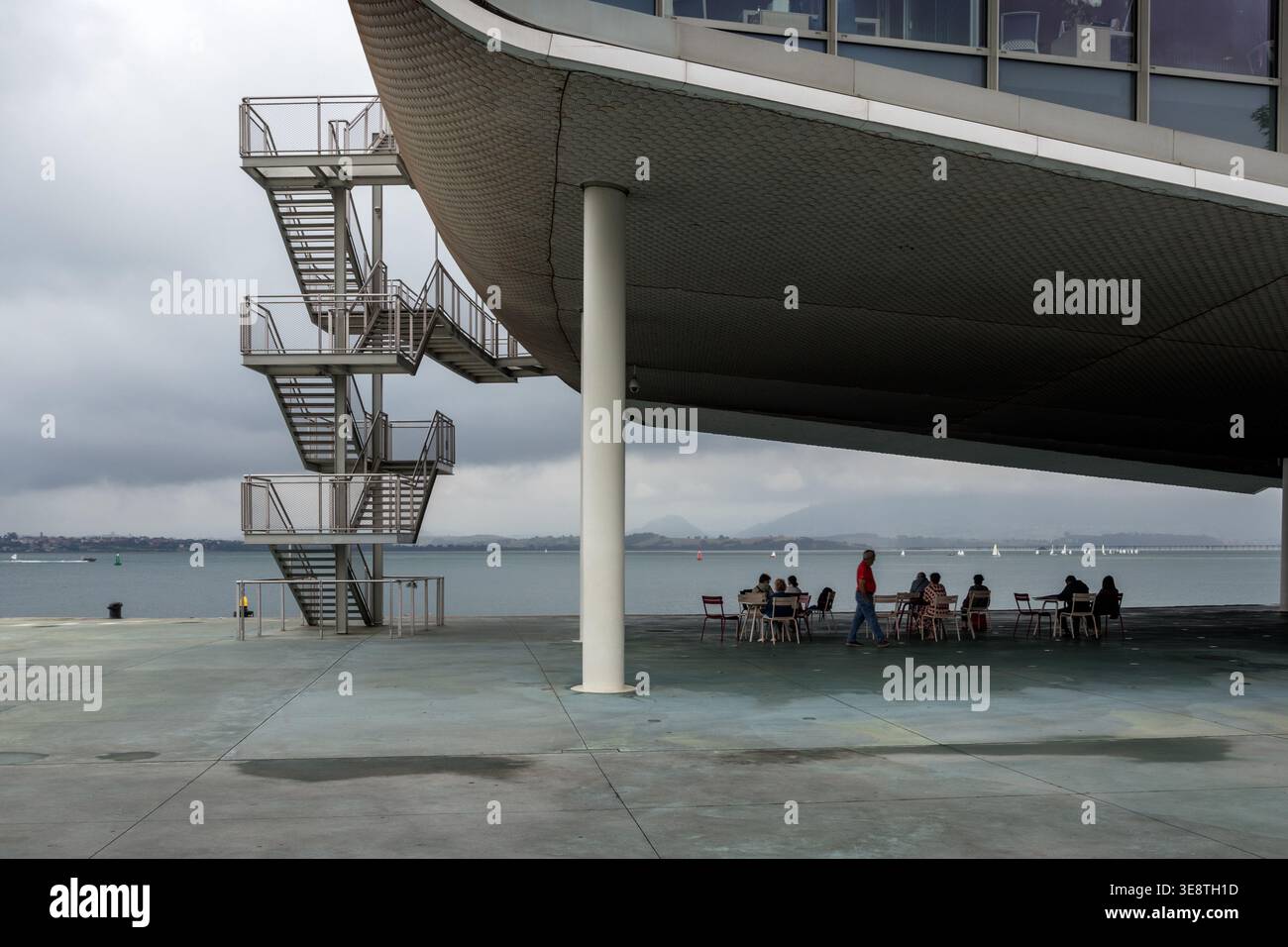 Santander, Spanien - 01. August 2024: Die Gäste entspannen auf einer Terrasse unter dem Centro Botín-Gebäude in Santander, Spanien. Hintergrundansicht der Santander Bay Stockfoto