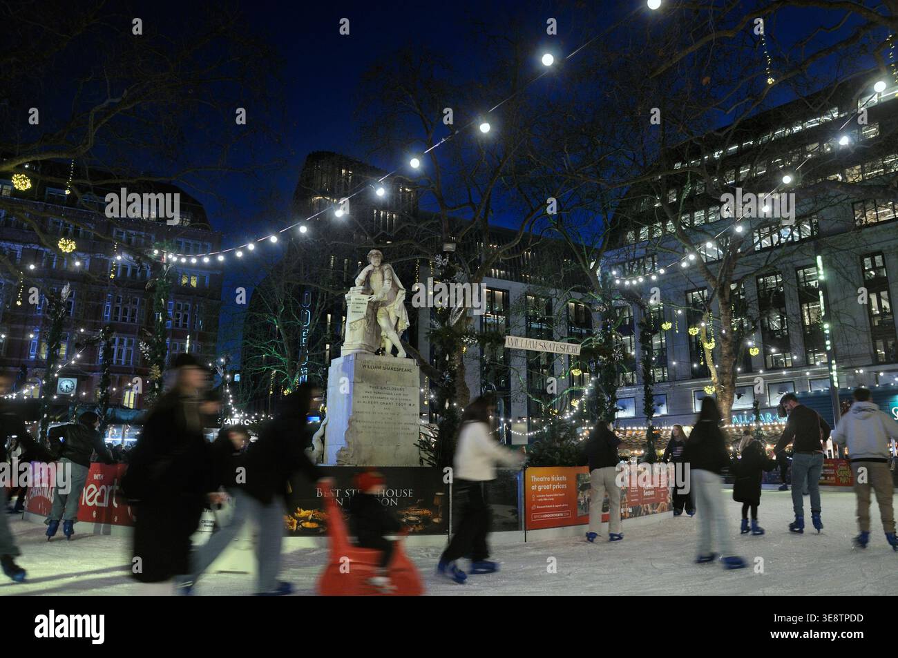 Im Winter können Besucher Schlittschuhlaufen am Skate Leicester Square, einer Eislaufbahn rund um die William Shakespeare Statue, genießen. Weihnachtsmarkt, Märkte London UK Stockfoto