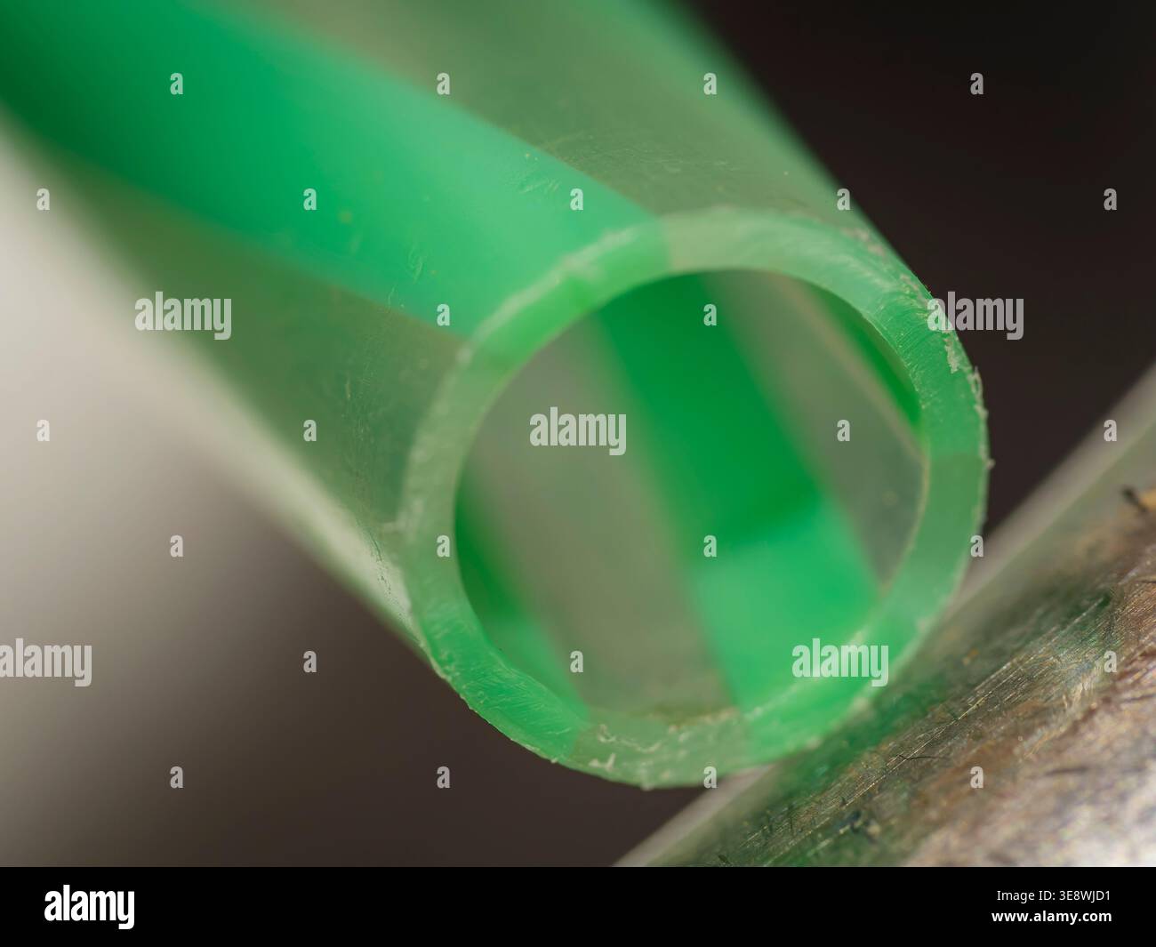 Makrofoto eines grün-weiß gestreiften Kunststofftrinkstrohschnittes, das sich gegen eine metallische Oberfläche lehnt. Stockfoto