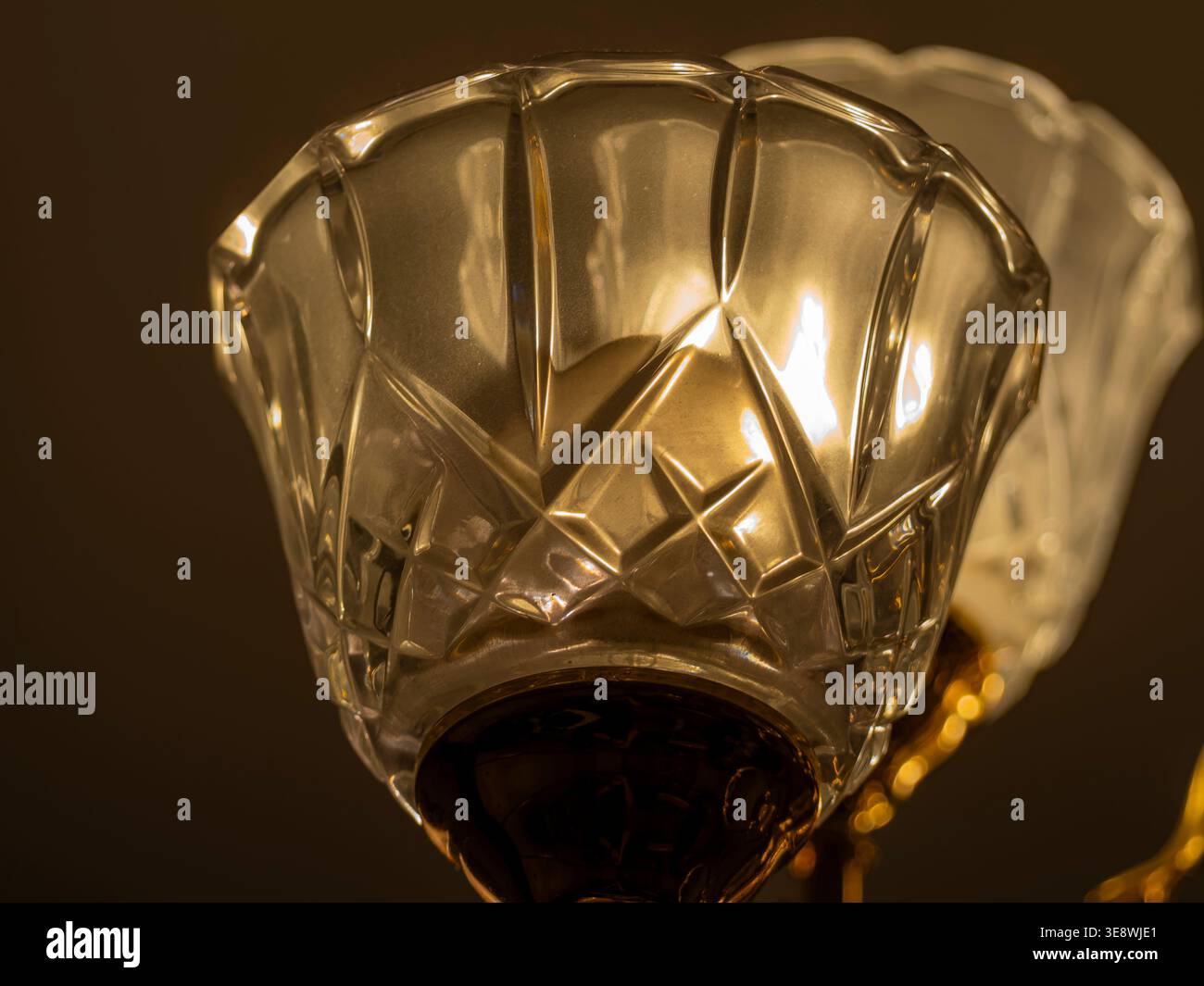Eleganter Lampenschirm aus Vintage-Kristallglas mit komplexen geometrischen Mustern, die mit warmem Bernsteinlicht vor dunklem Hintergrund leuchten Stockfoto