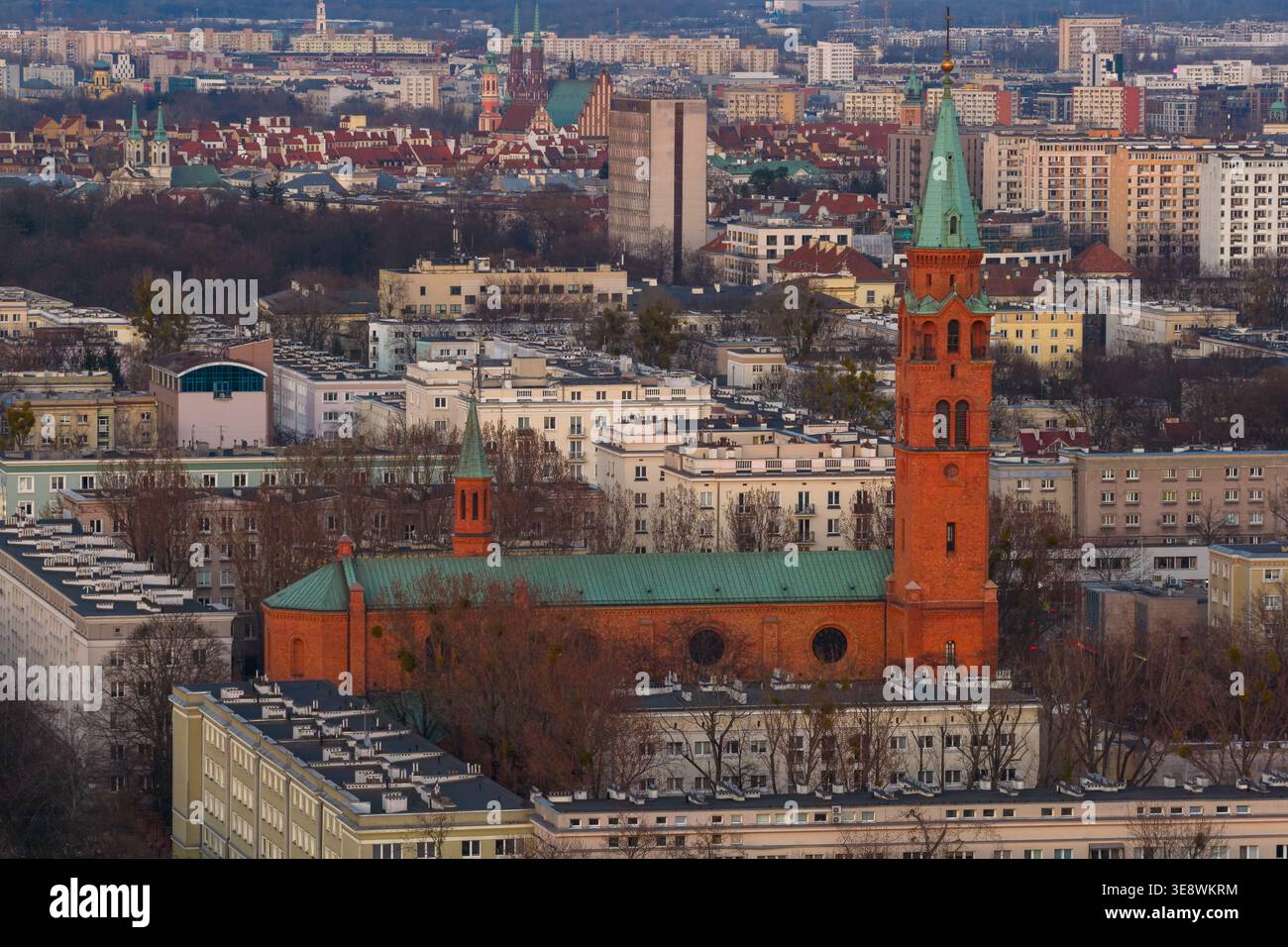 Blick aus der Vogelperspektive auf die historische Augustinerkirche mit ihrem hohen grünen Turm und der roten Backsteinfassade, umgeben von städtischen Wohngebäuden in Warschau, Stockfoto