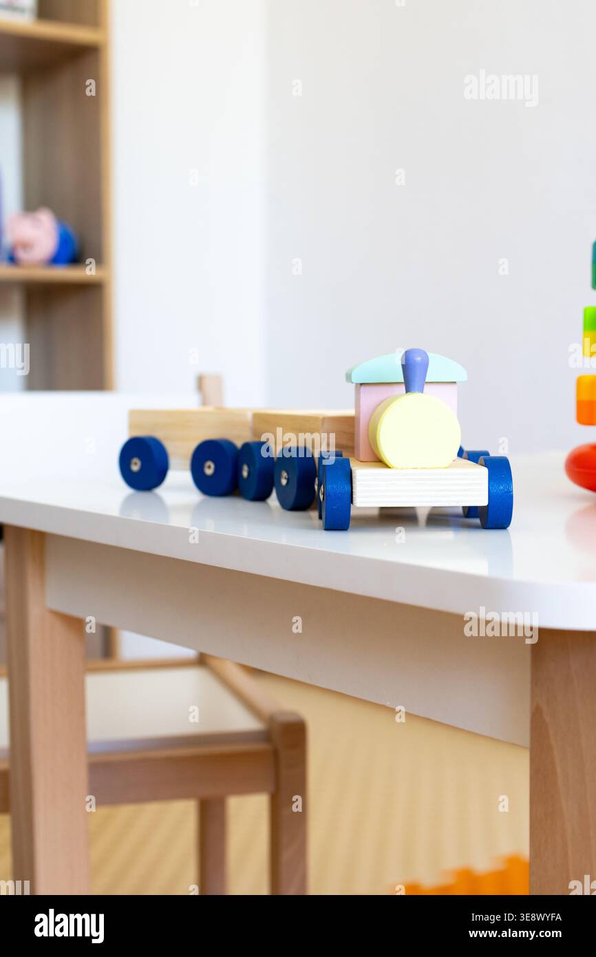 Niedriger Winkel einer kleinen Holzlokomotive mit blauen Rädern, die zwei Wagen auf einem Kinderpult führen, mit schlichtem Design und robusten Materialien Stockfoto