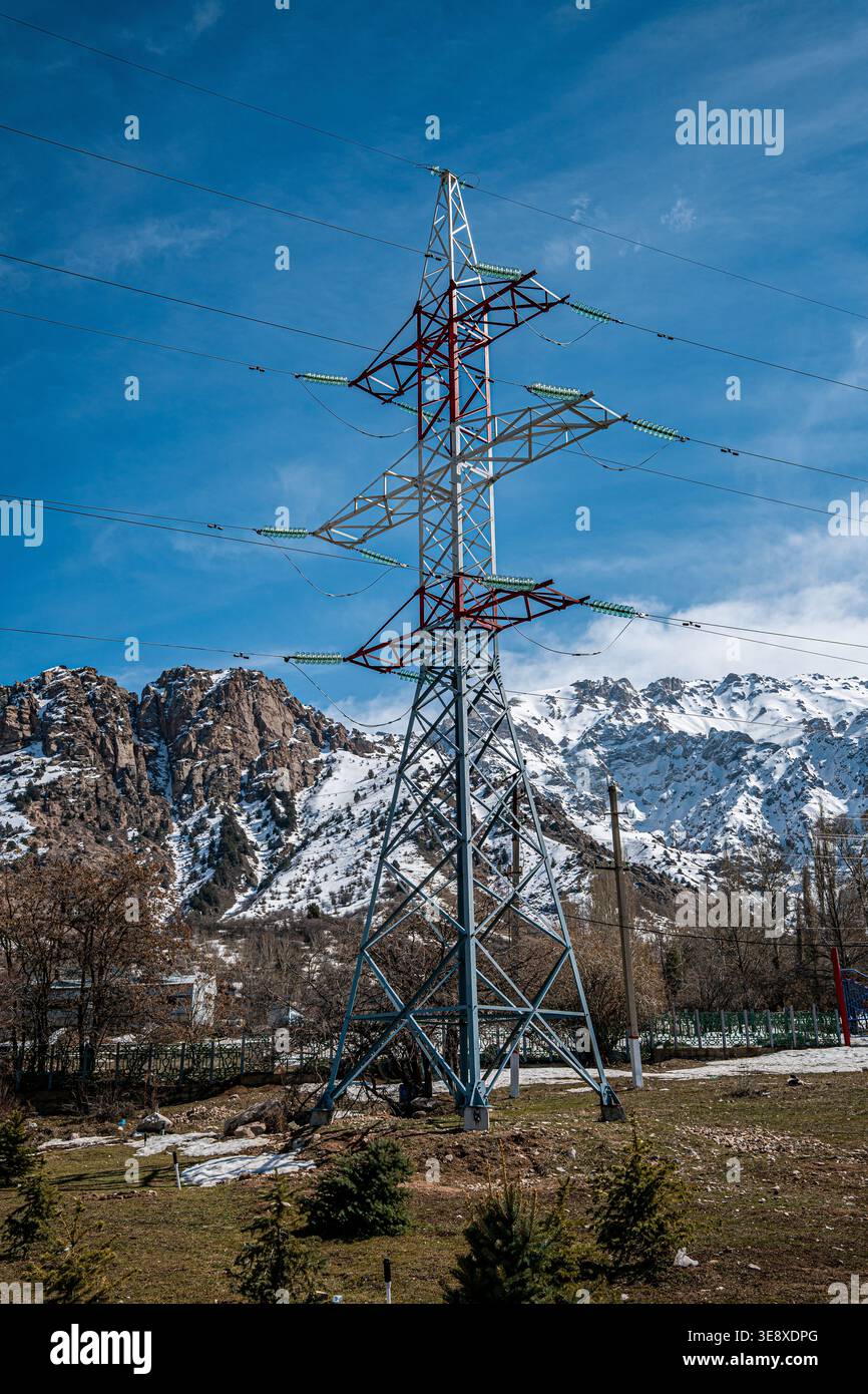 Ein hoher Turm der Stromleitung steht vor der Kulisse schneebedeckter Berge und eines klaren blauen Himmels, der die Kreuzung von Natur und Infrastruktur darstellt. Stockfoto