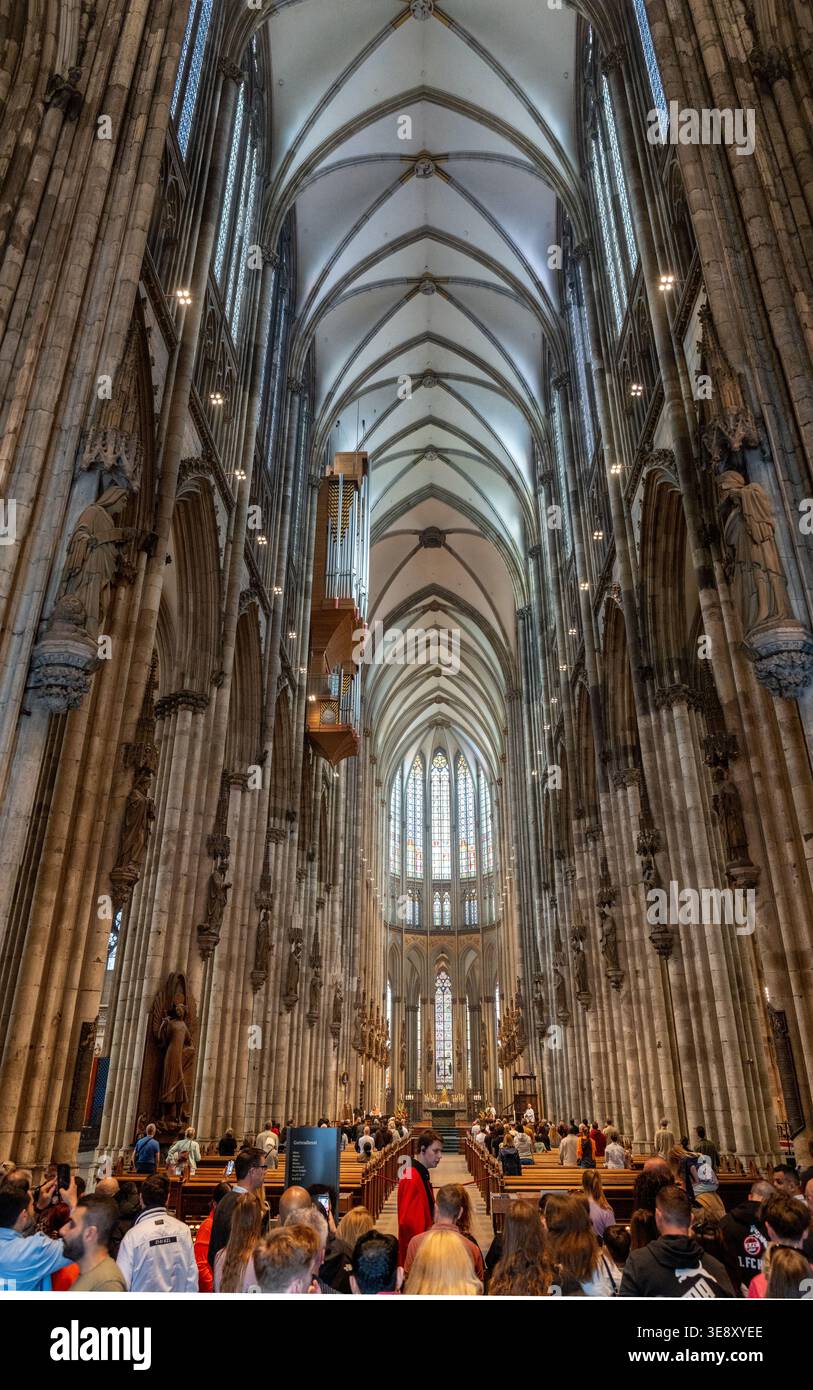 Weite Innenansicht des Kirchenschiffs im Kölner Dom mit Rippengewölben, Säulen und Besuchern in Köln. Stockfoto