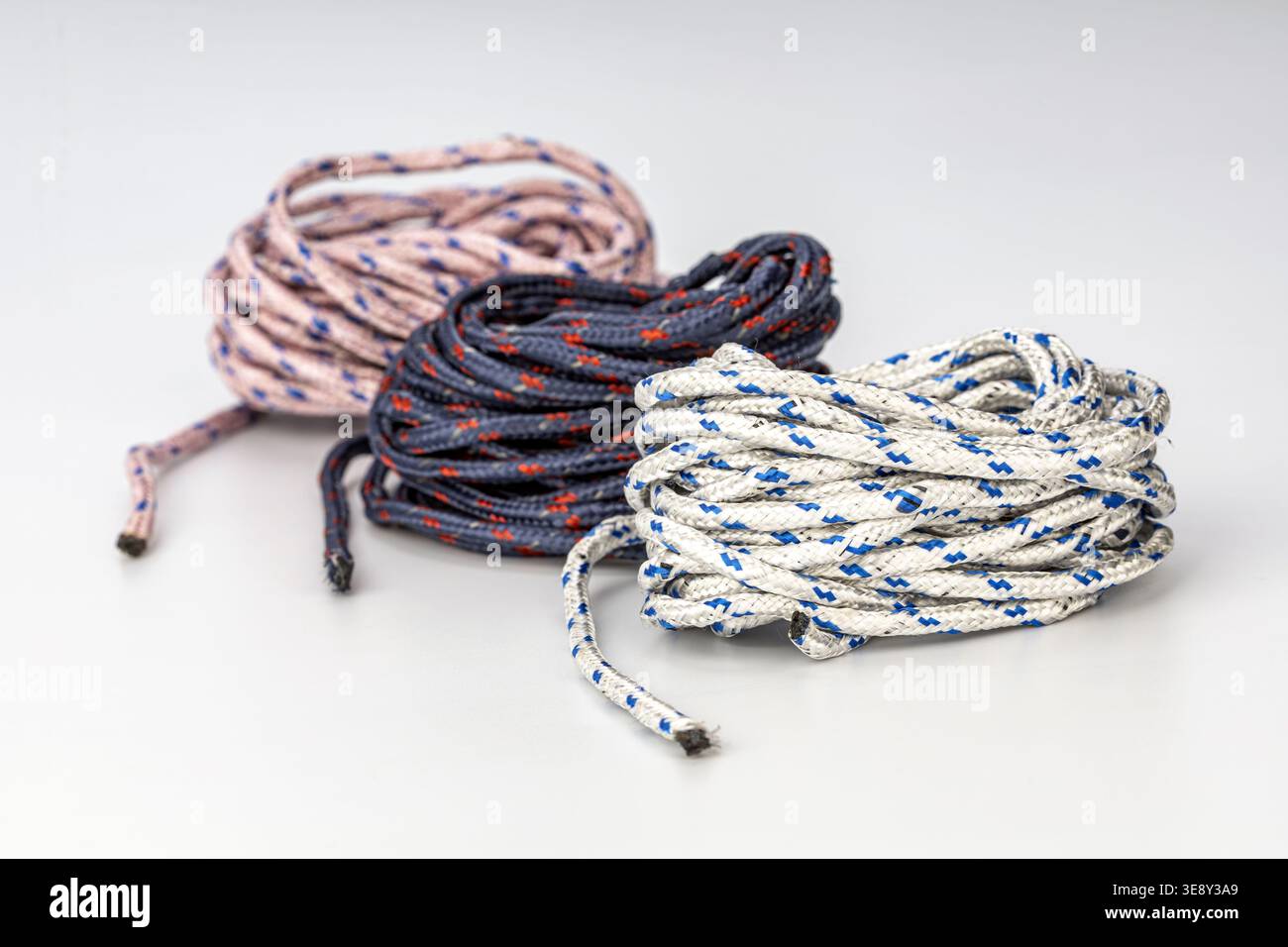 Drei professionell angeordnete geflochtene Nylonseile mit unterschiedlichen Farbschemata: Weiß mit blauen Streifen, schwarz mit roten Akzenten und grau W Stockfoto