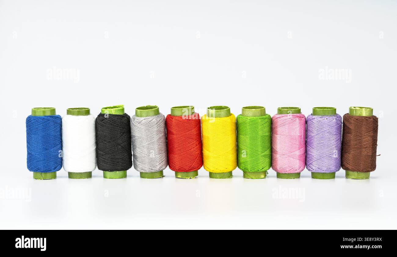 Zehn bunte Fadenspulen, die ordentlich in einer geraden Linie angeordnet sind, mit leuchtendem Blau, weiß, Schwarz, Grau, rot, gelb, hellgrün, rosa, p Stockfoto