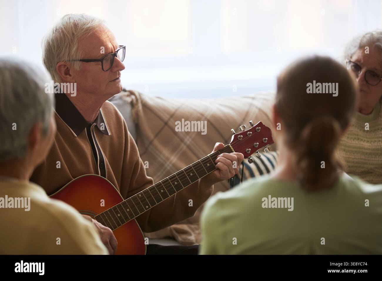 Senior-Mann spielt Gitarre während Gruppensitzungen im Pflegeheim, unterstützt soziales Engagement und emotionale Betreuung Stockfoto