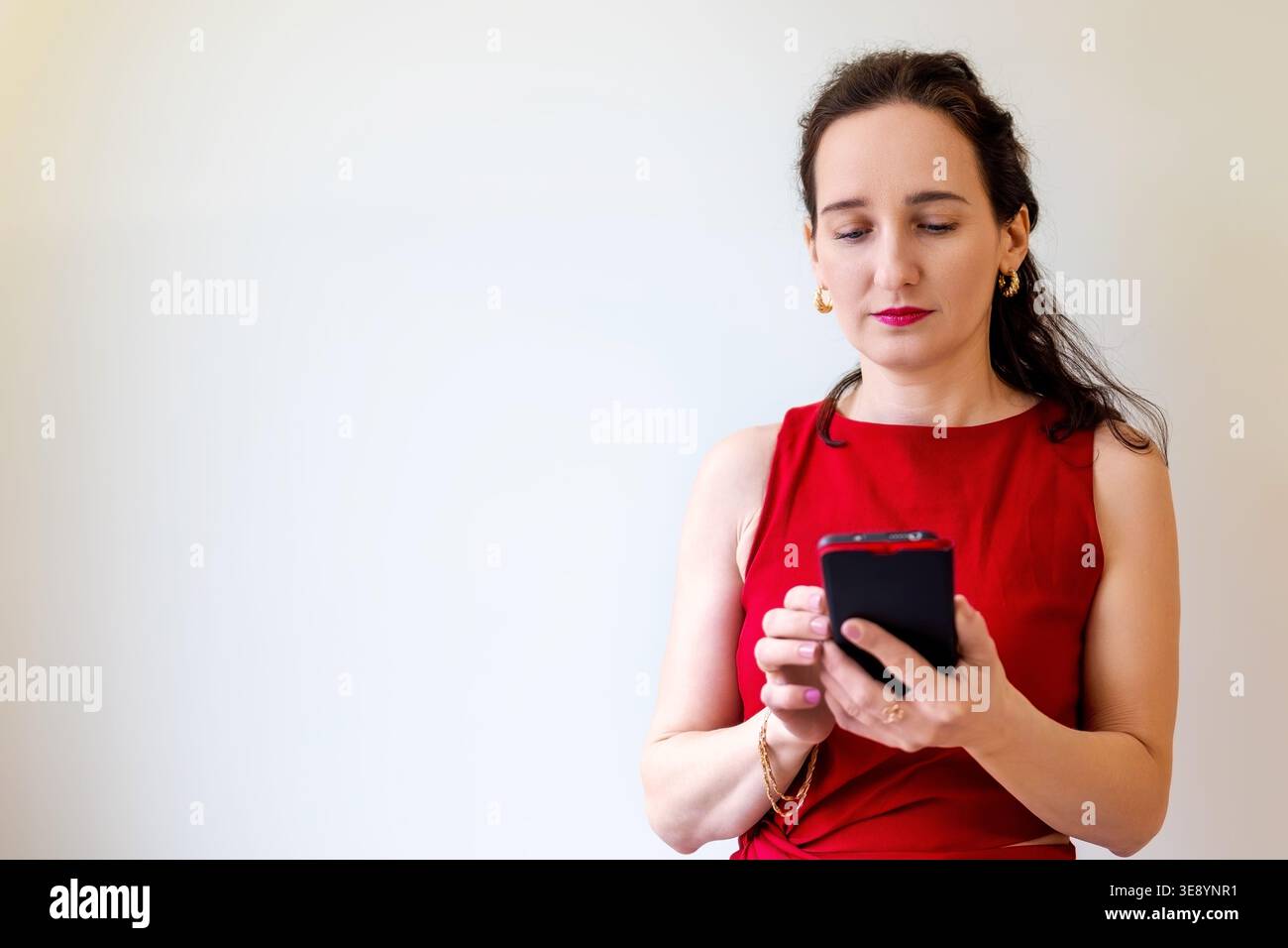 Frau in rotem Kleid mit Smartphone, fokussierter Ausdruck beim SMS oder Surfen auf einem mobilen Gerät. Leerzeichen für Text. Stockfoto