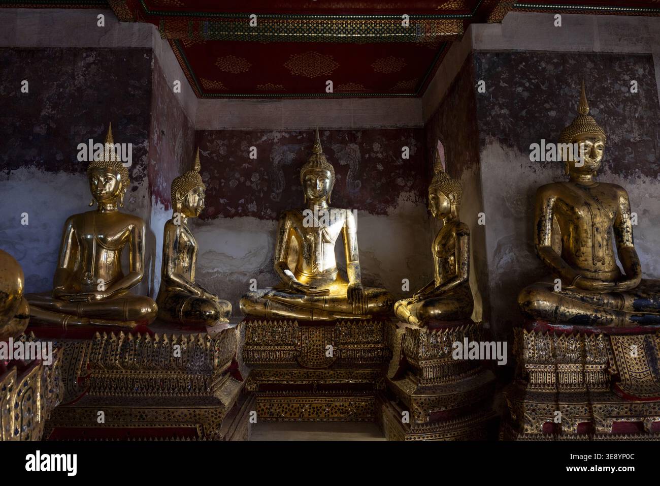 Goldene Buddha-Statue, die im antiken dunklen Tempelraum sitzt und friedliche spirituelle Emotionen mit verblasstem gemalten Wandhintergrund zeigt, der sanft unter leuchtet Stockfoto