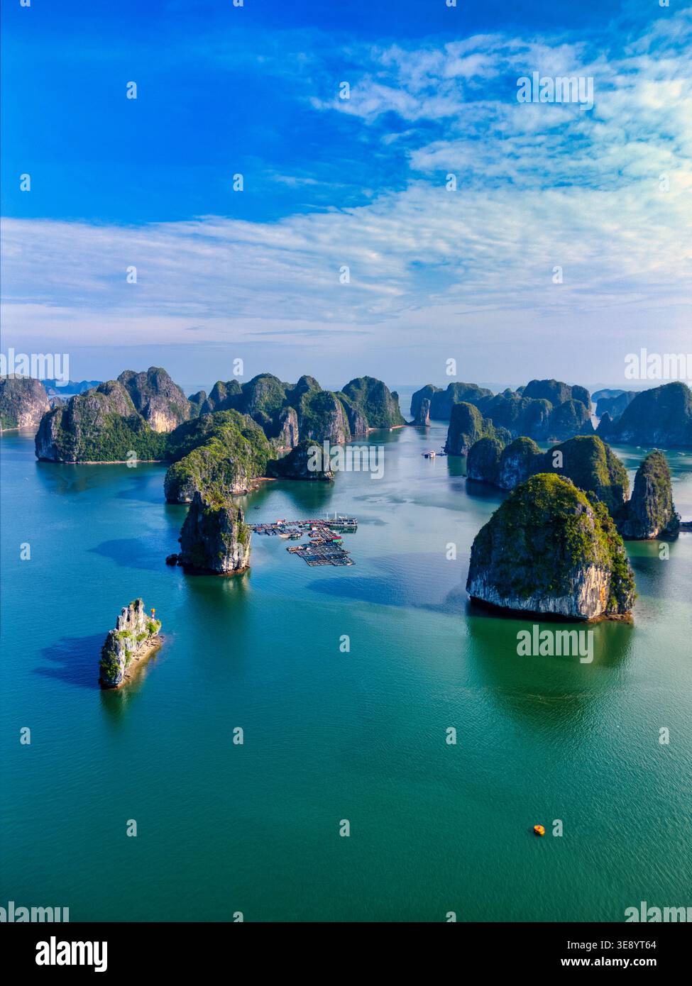 Aus der Vogelperspektive auf Kalksteinkarste des Cat Ba Archipels, die aus türkisfarbenem Wasser mit schwimmenden Fischfarmen unter einem klaren blauen Himmel aufsteigen: Ha Tu, Hai Phong, Vietnam Stockfoto