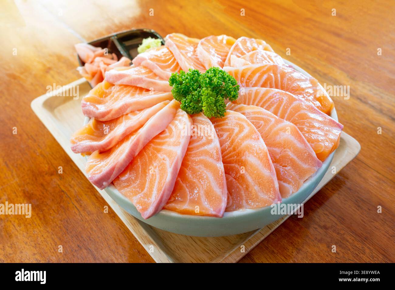 Köstliche Nahaufnahme frischer Lachs-Sashimi-Scheiben, die in einer kreisförmigen Schüssel auf einem Holztablett angeordnet sind, mit komplizierten Mustern aus Orange und weiß f Stockfoto