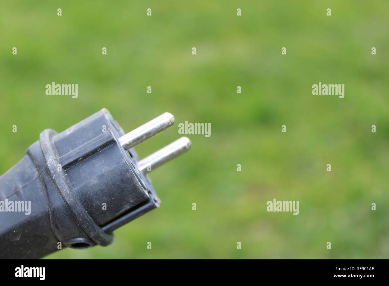 Die Nahaufnahme eines Steckers mit zwei Metallkontakten hebt sich vor einem grünen Grashintergrund ab. Diese Szene wird an einem sonnigen Tag aufgenommen. Stockfoto