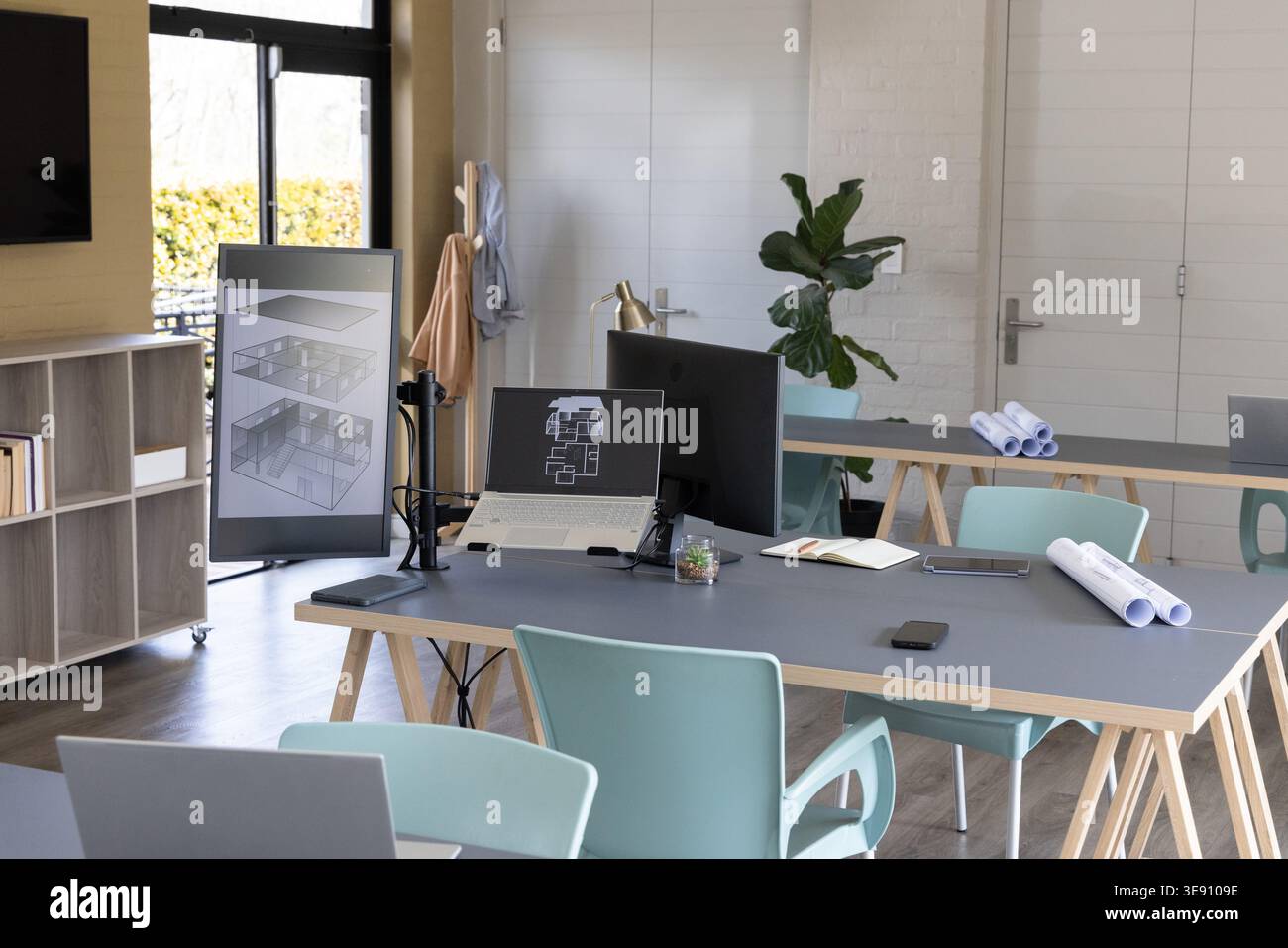 Tabelle der zentralen Arbeitsstation mit Architekturplänen auf dem Laptop und dem vertikalen Monitor im Studio. Konstruktion, Zeichnungserstellung, Renderings, Blueprints, Modellierung, Co Stockfoto