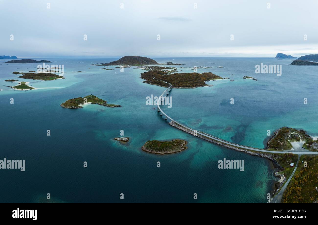 Aus der Vogelperspektive der Sommaroy Bridge, die kleine Inseln mit türkisfarbenem Wasser und Herbstlaub unter einem bewölkten Himmel in Sommaroy, Troms, Norwegen verbindet. Stockfoto