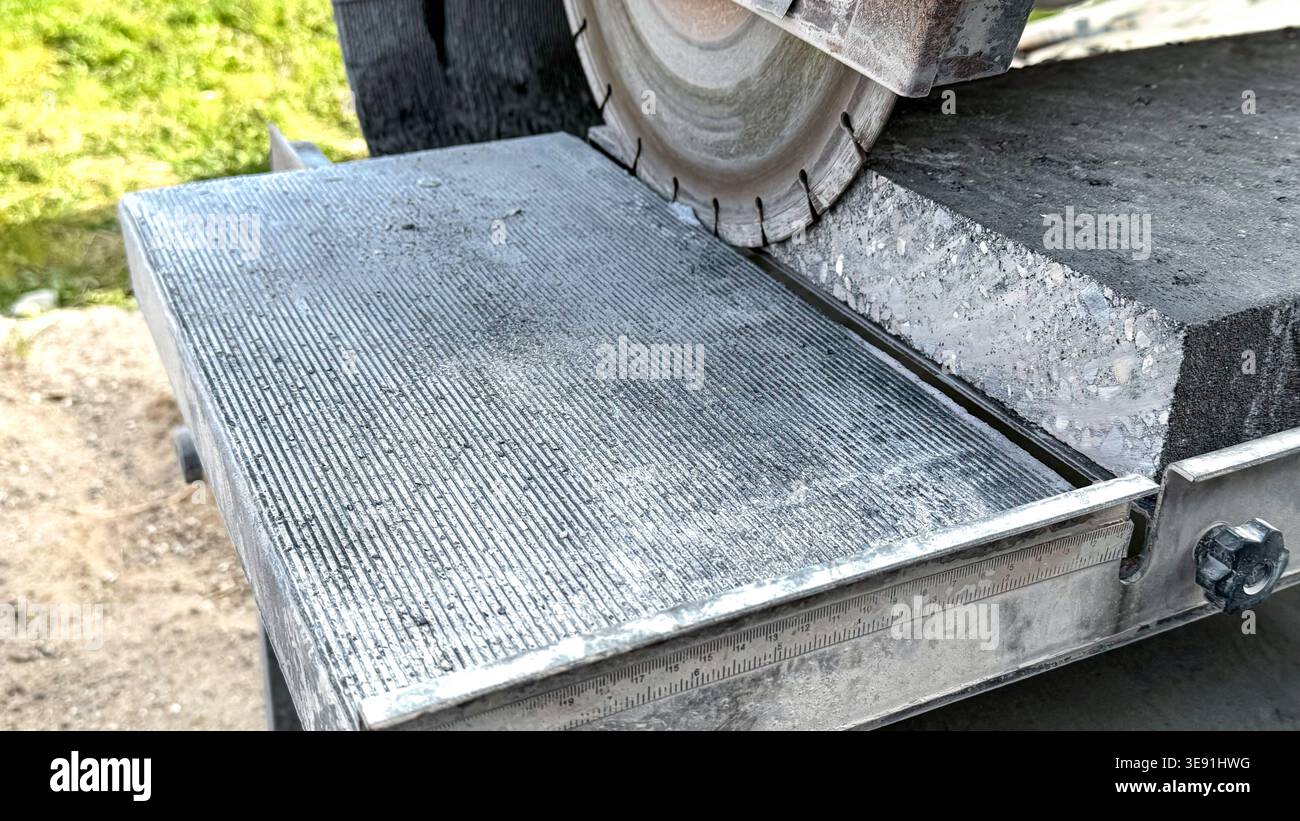 Betonschneidemaschine mit Diamantklinge, die über einer Platte positioniert ist und Präzisionsschneidewerkzeuge und Messmarkierungen auf der Metallführung zeigt Stockfoto