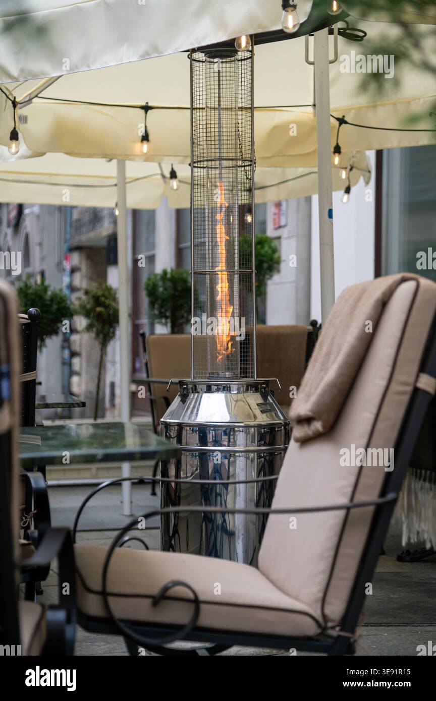 Eine Gruppe von Stühlen sitzt um eine Heizung in einem Café im Freien, während die Lichter darüber hängen. Stockfoto