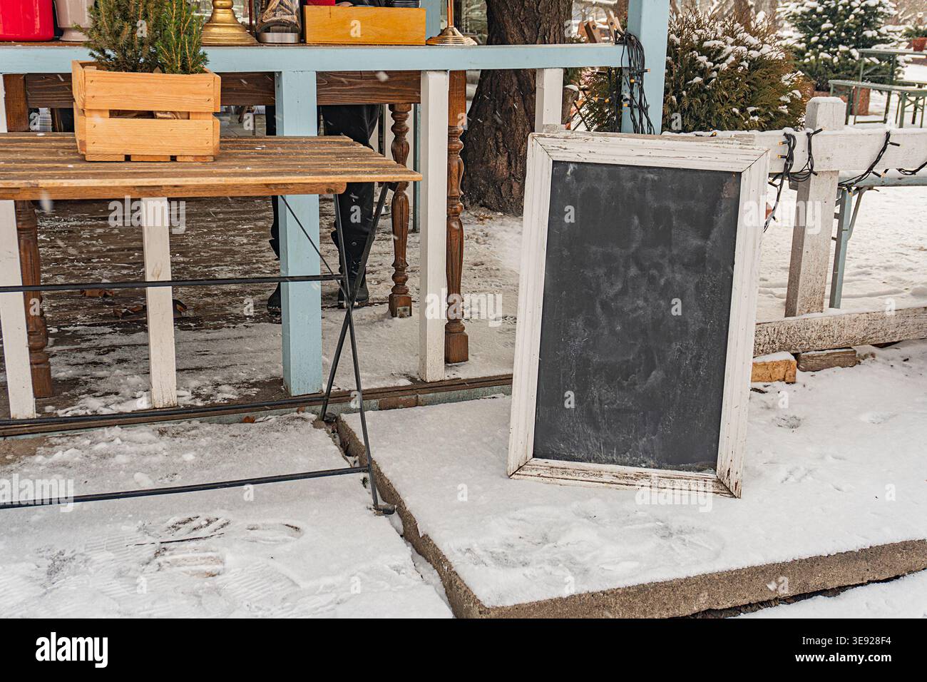 Verschneite Outdoor-Szene mit einem Holztisch in der Nähe eines Zauns Eine Tafel steht zentral, leer und gut gepflegt vor der verschneiten Kulisse unter weichem Licht Stockfoto