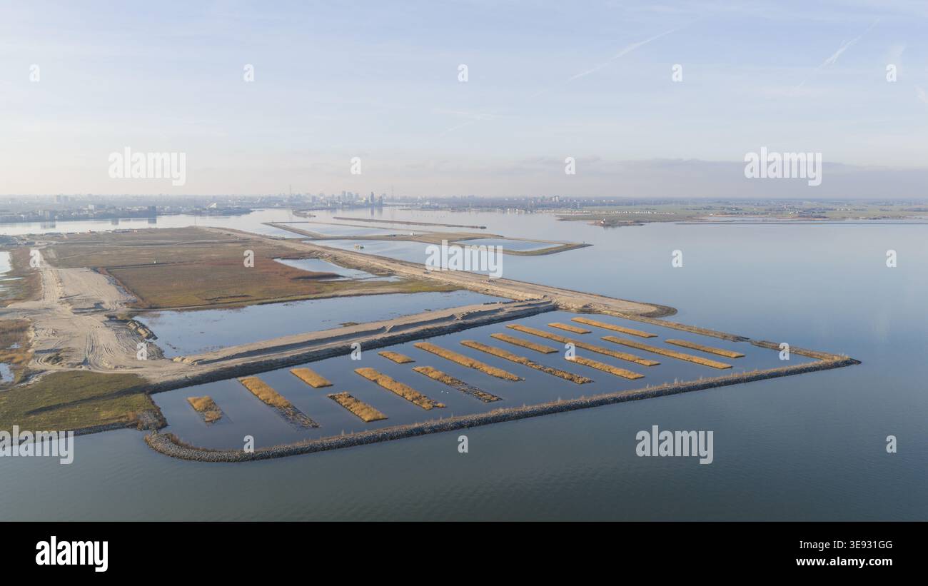 Aus der Vogelperspektive auf die Baustelle Sportpark Strandeiland mit rechteckigen Wasserbecken und Sandbänken unter klarem Himmel mit der Skyline der Stadt Stockfoto