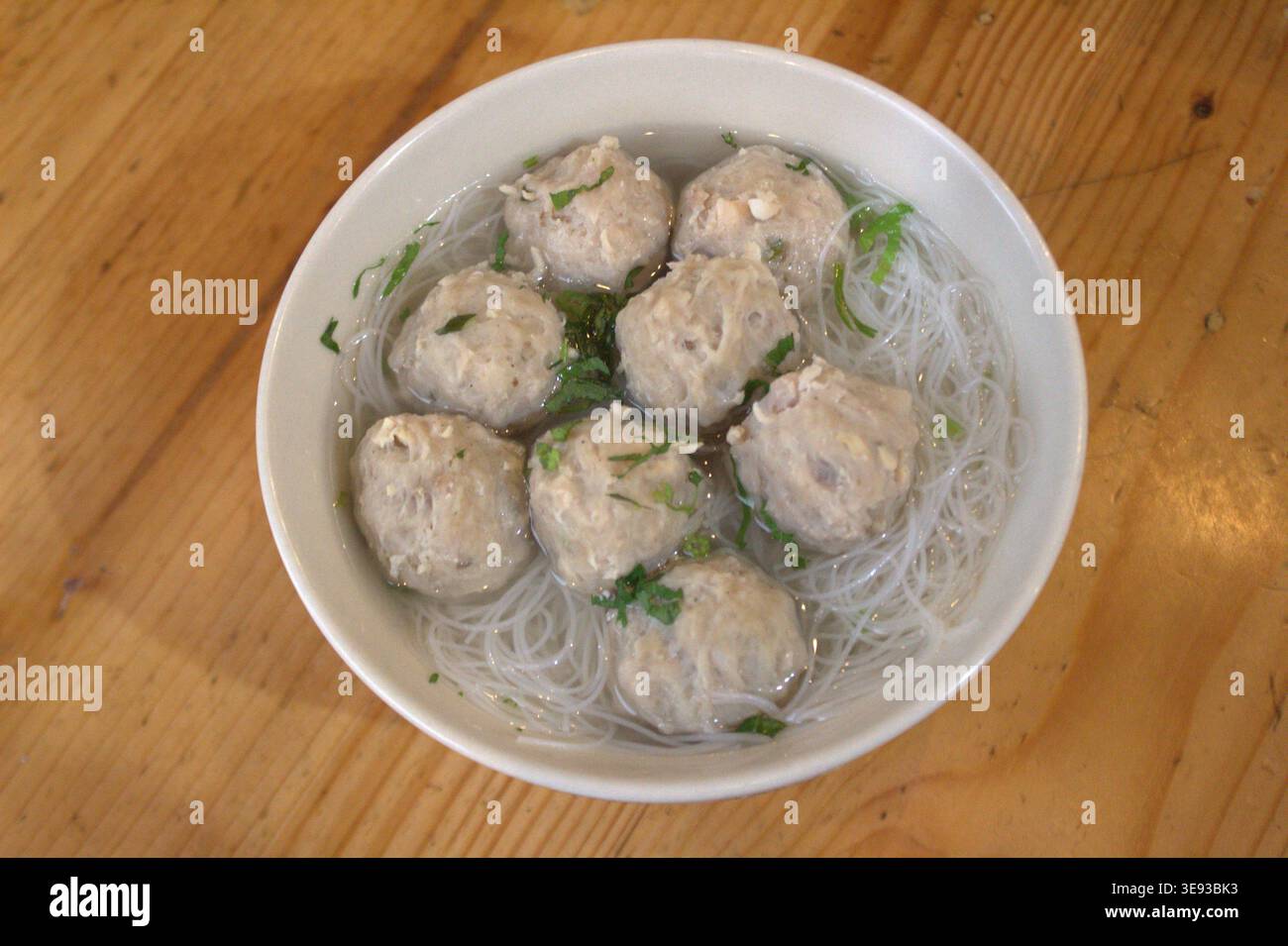 Eine Schüssel mit Fleischbällchen mit Reisvermicelli und Gemüse auf einem Holztisch Stockfoto