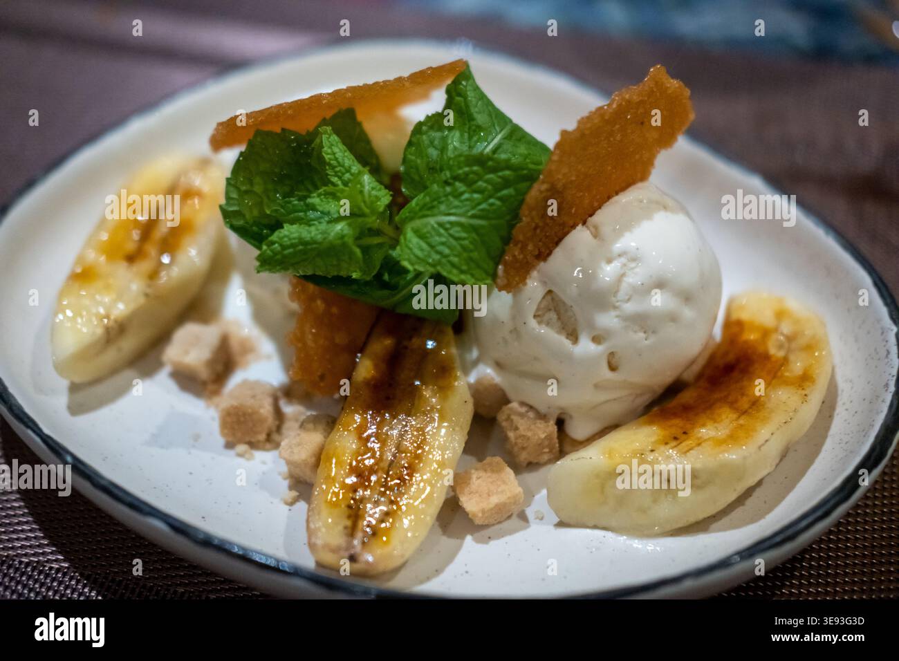 Karamellisiertes Bananendessert mit Vanilleeis, Minzblättern und knuspriger Zuckergarnitur auf einem Teller. Stockfoto