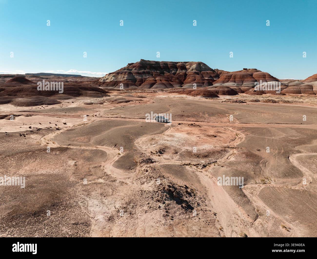 Aus der Vogelperspektive eines weißen Fahrzeugs, das durch die bunt gestreiften Bentonite Hills unter einem klaren blauen Himmel in Hanksville, Utah, USA fährt. Stockfoto