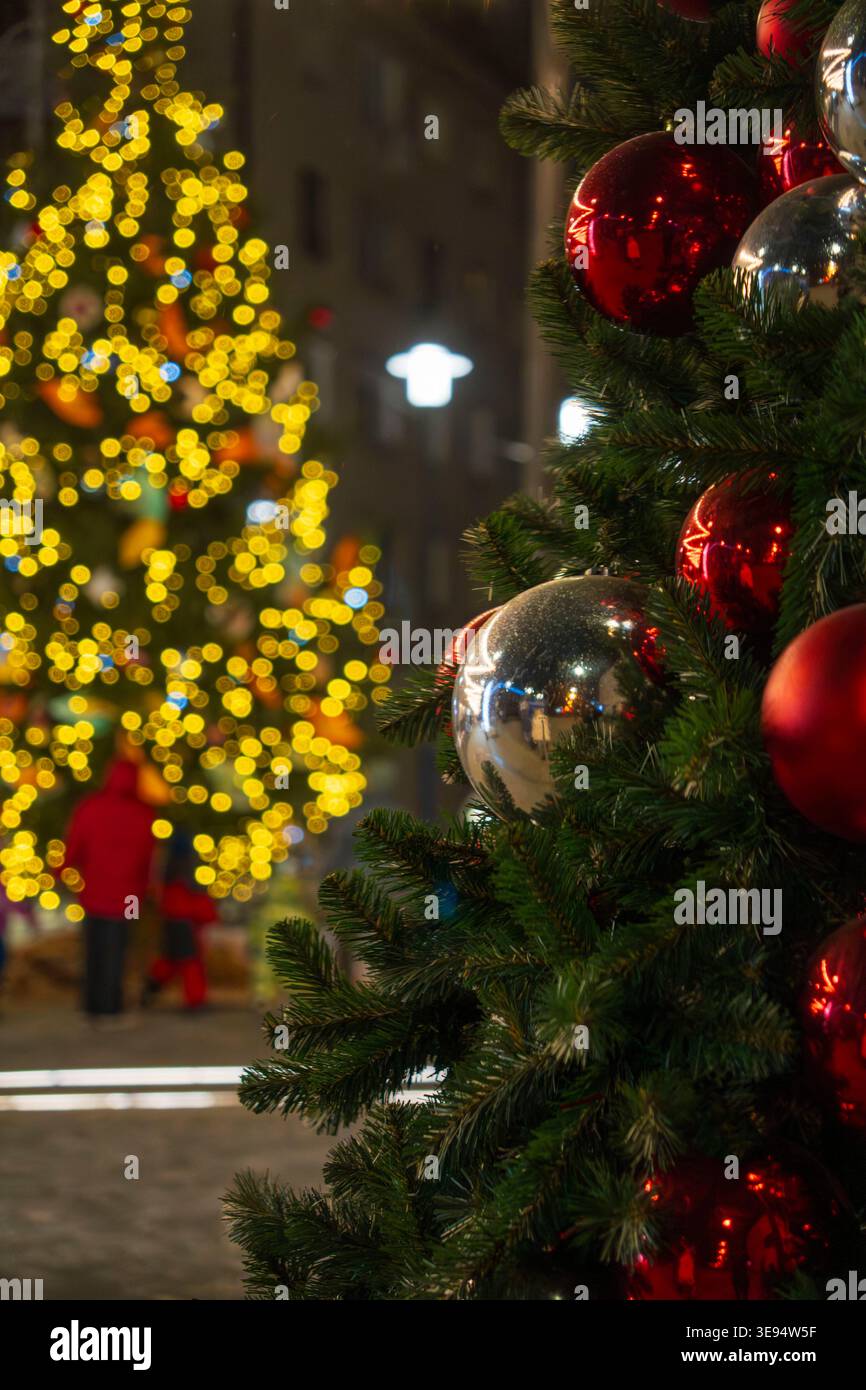 Im Vordergrund steht ein wunderschön dekorierter Weihnachtsbaum mit roten und silbernen Ornamenten, beleuchtet von warmen festlichen Lichtern. Im Hintergrund Stockfoto